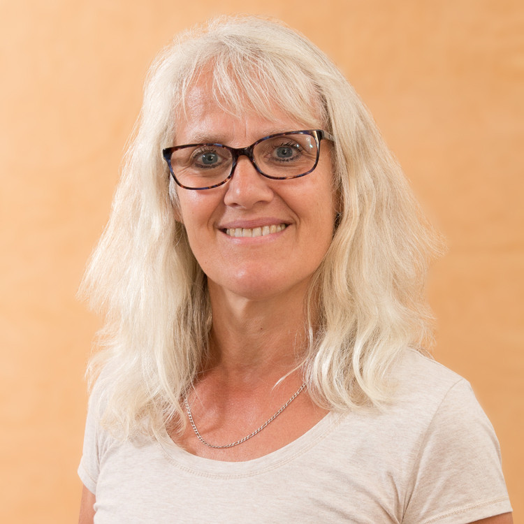 Brigitte Knöpfle mit weißem Haar und hellem T-Shirt vor beigem Hintergrund