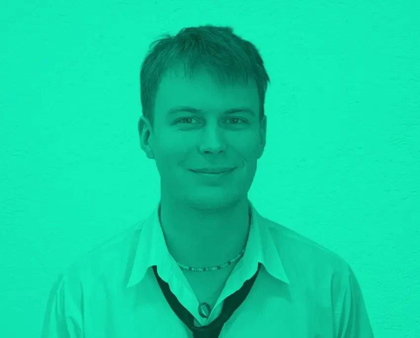 Person namens Colin mit offenem Hemd und Krawatte vor grünem Hintergrund