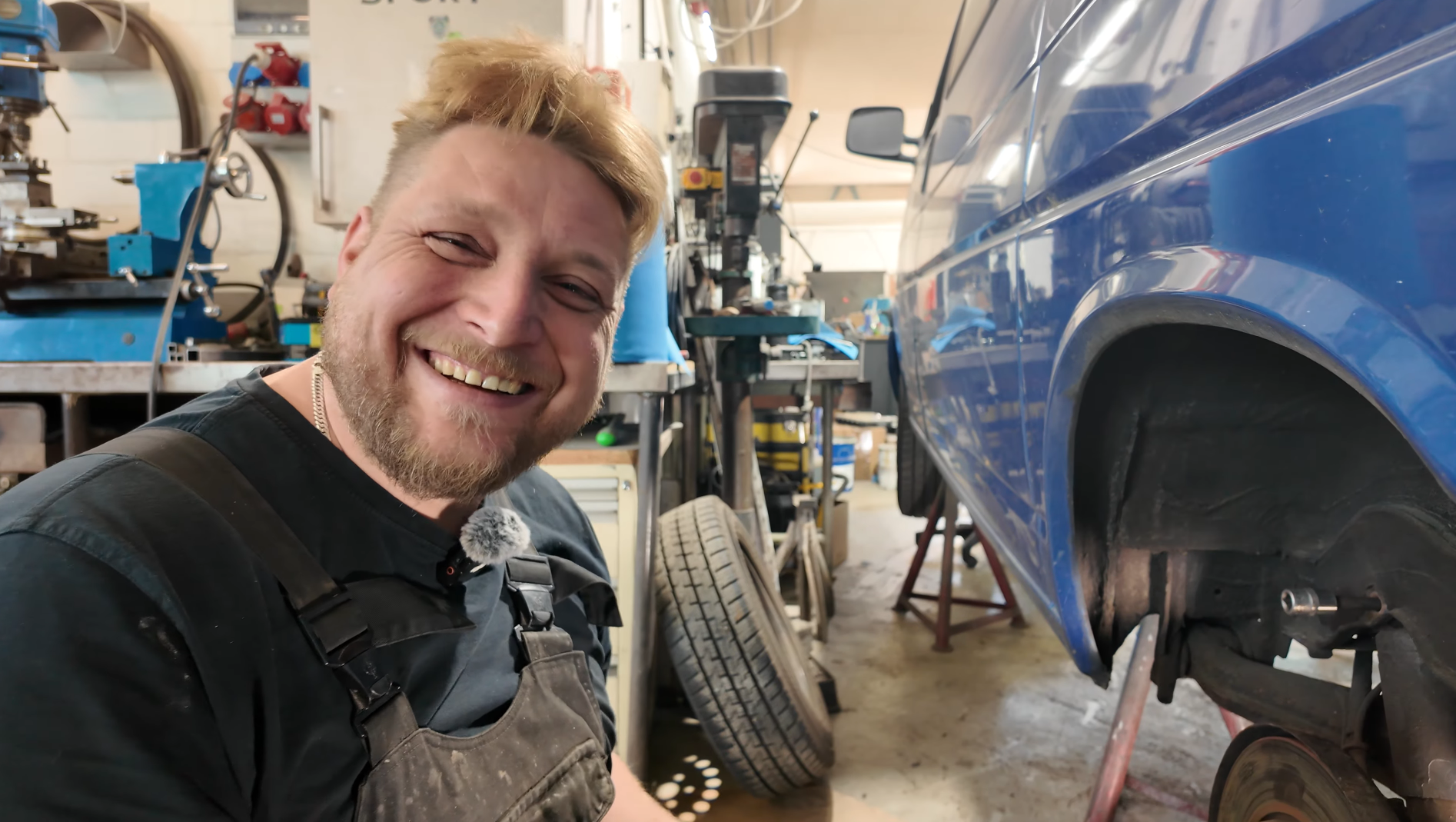 Mechaniker arbeitet in einer Autowerkstatt neben einem blauen Fahrzeug aufgebockt auf Wagenheber