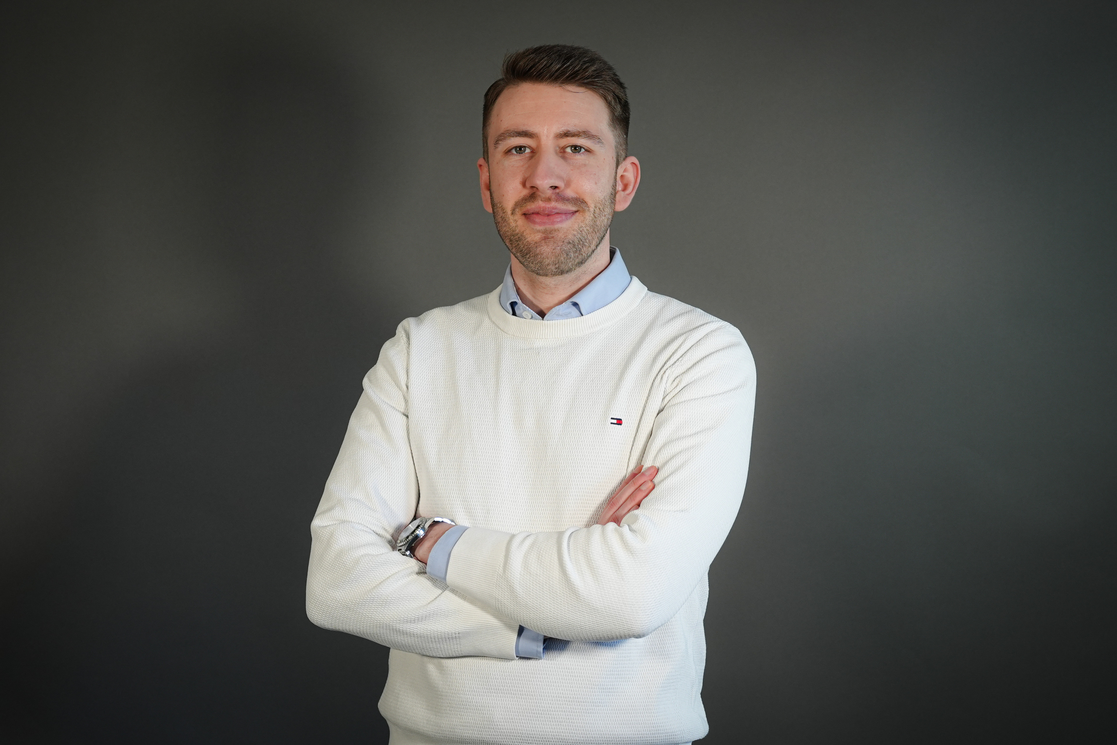 Nicolai Müller im weißen Pullover mit verschränkten Armen vor grauem Hintergrund