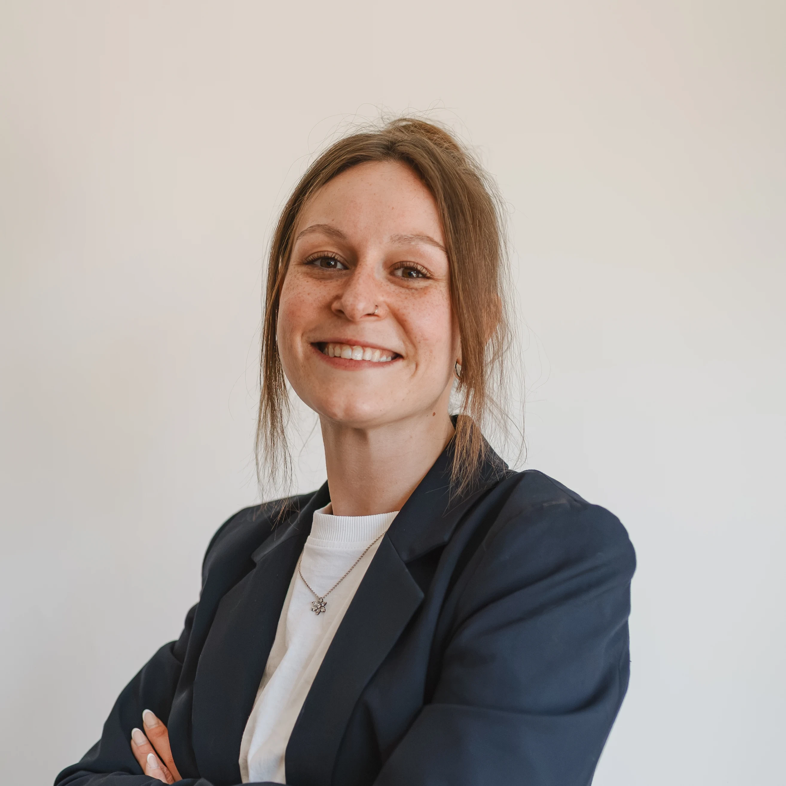 Portrait von Malena Zacher, lächelnde Frau im Blazer vor hellem Hintergrund