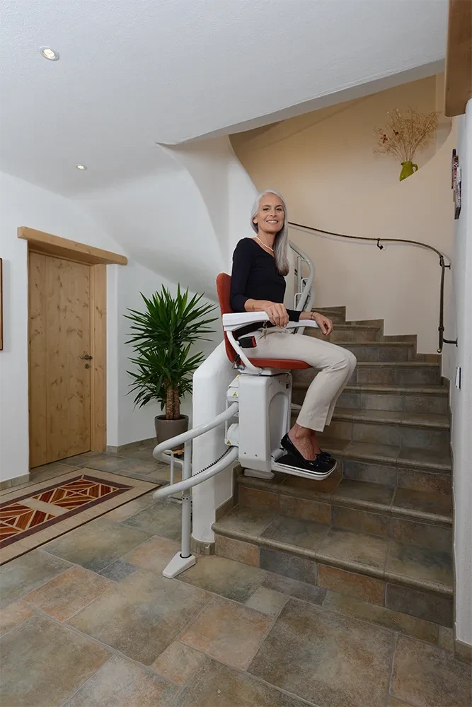 Treppenlift Alpha Classic im Einsatz auf einer Innentreppe mit sitzender Frau