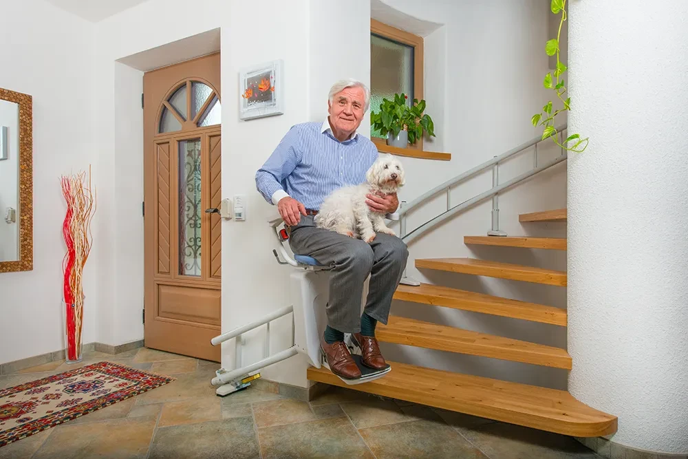 Treppenlift Alpha Premium für kurvige Treppen, älterer Mann mit Hund nutzt den Treppenlift im Haus