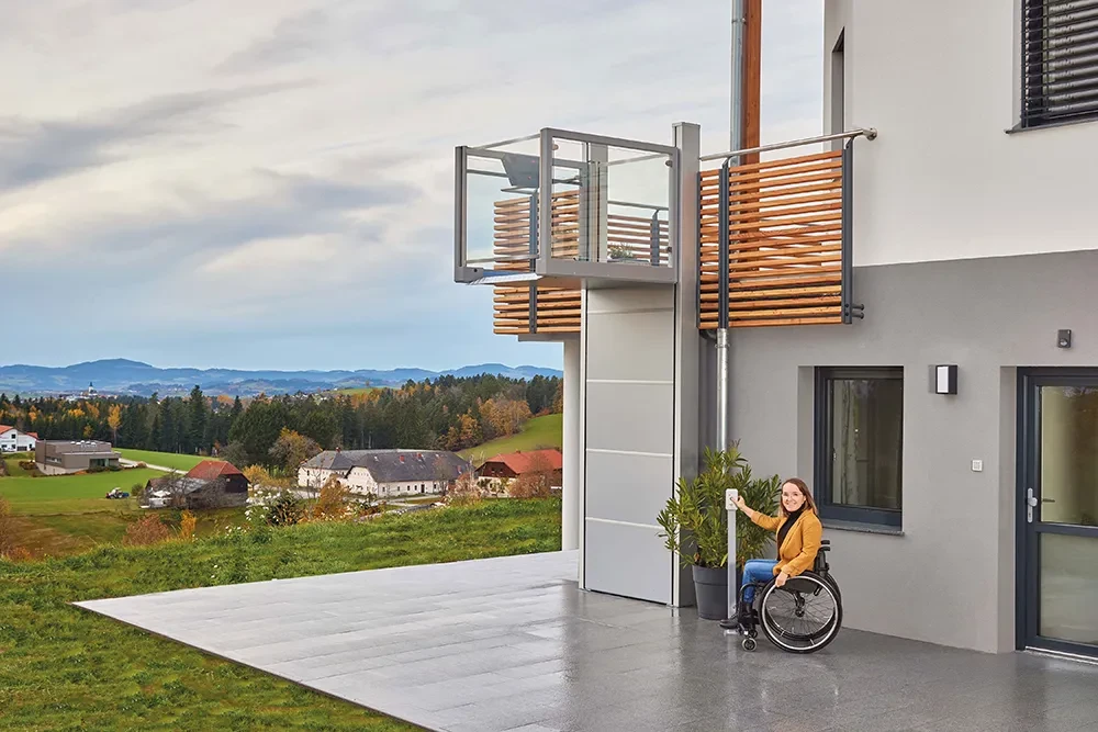 Frau im Rollstuhl nutzt die Ascendor Hebebühne Una Porte am Haus