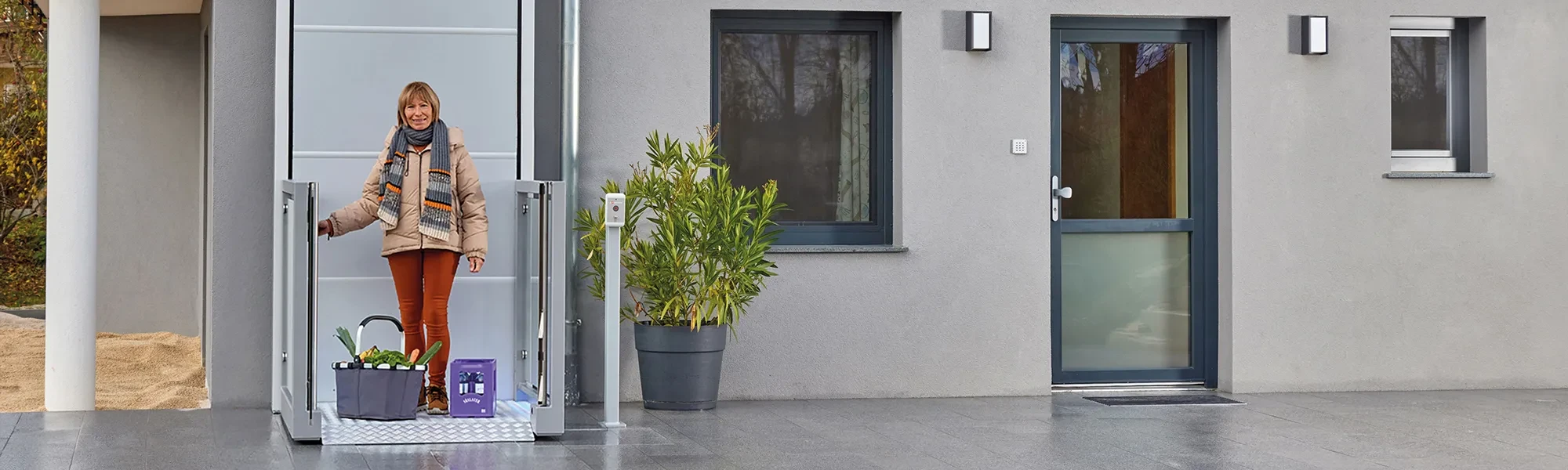 Moderner Hauseingang mit Service-Element, graue Fassade, Fenster und Pflanze im Topf