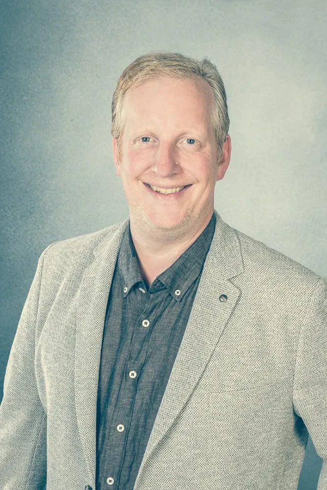 Porträt von Heilpraktiker Jan Tiedau in grauem Sakko vor neutralem Hintergrund