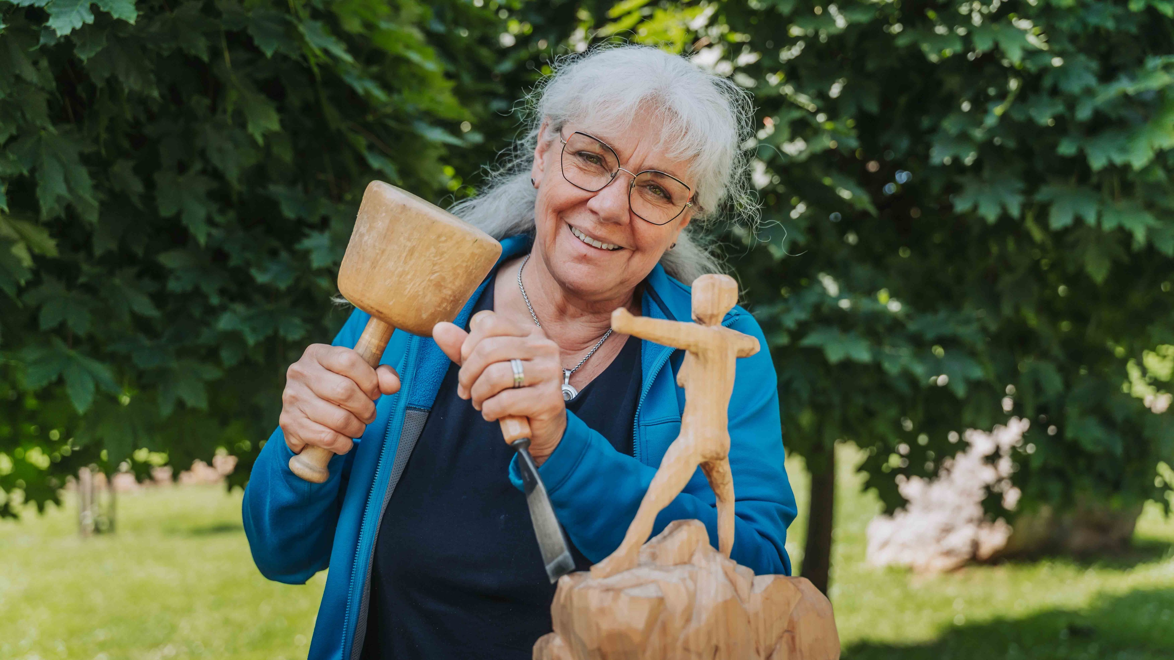 Frau beim Holzschnitzen einer Figur im Freien, alea alternativ s 21