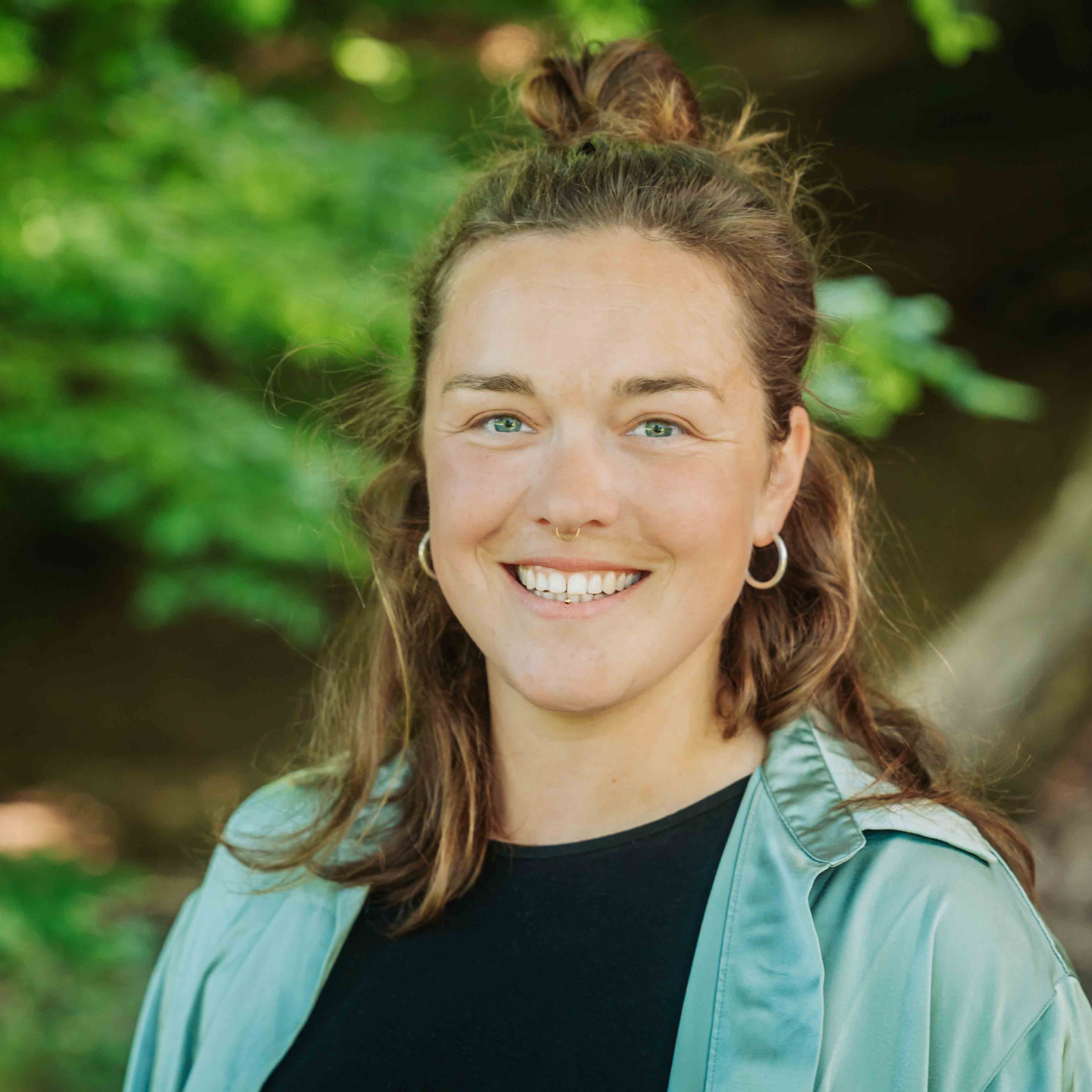 Alea Portrait im Grünen, Frau mit langen braunen Haaren und türkisfarbener Jacke