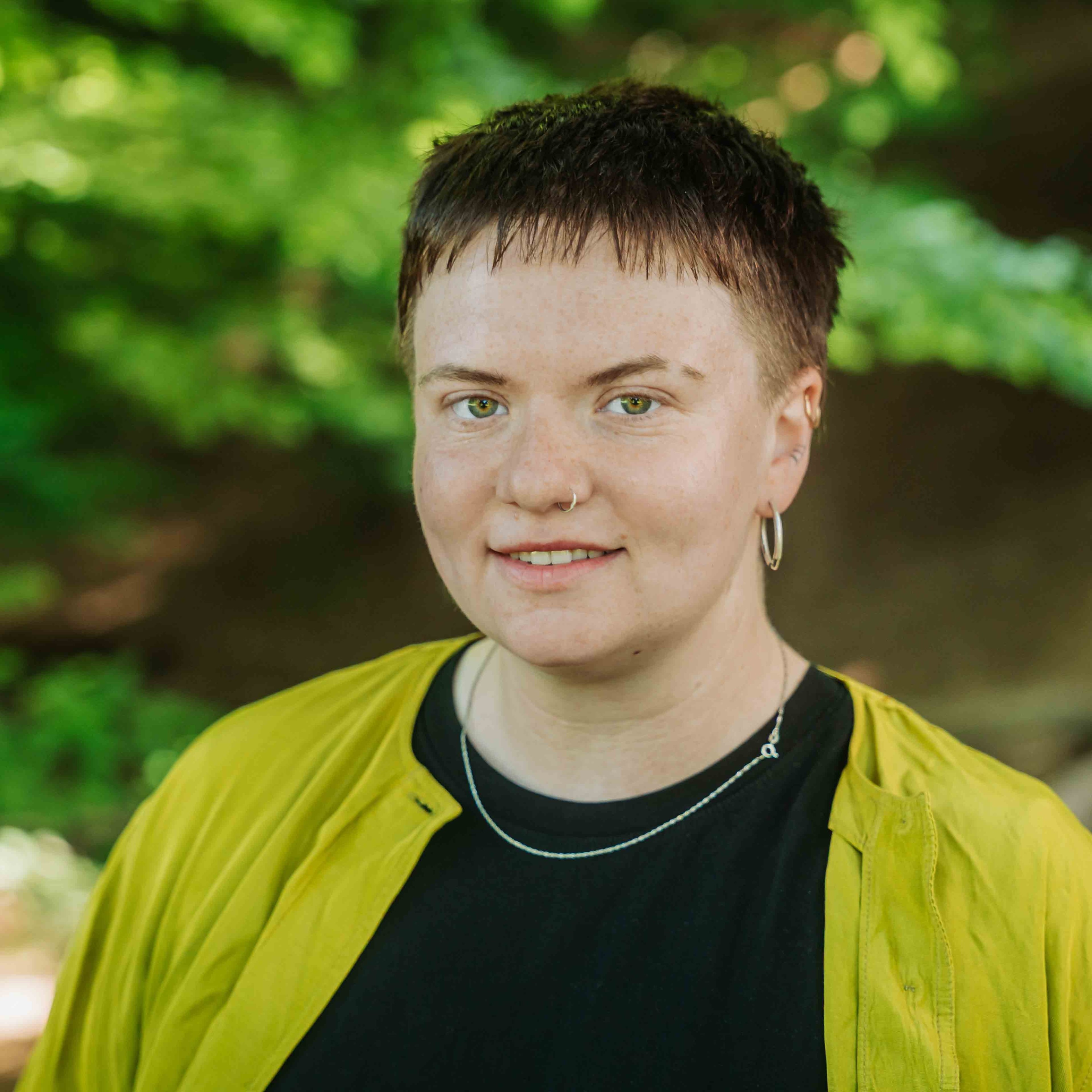 Alea Portrait im Grünen mit gelber Jacke und kurzem Haar