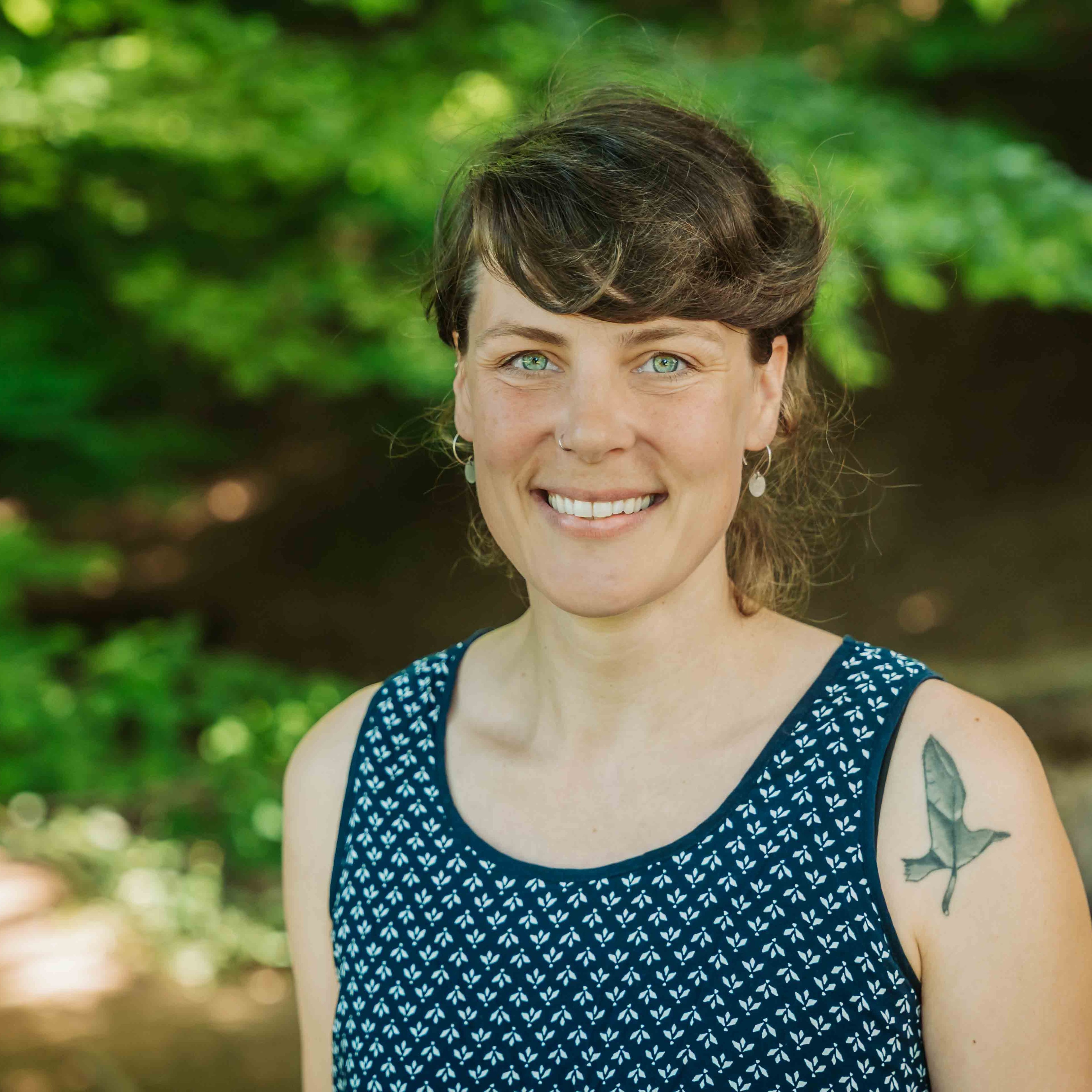 Alea Portrait im Sommer mit Tattoo am Arm und blauem Kleid im Grünen