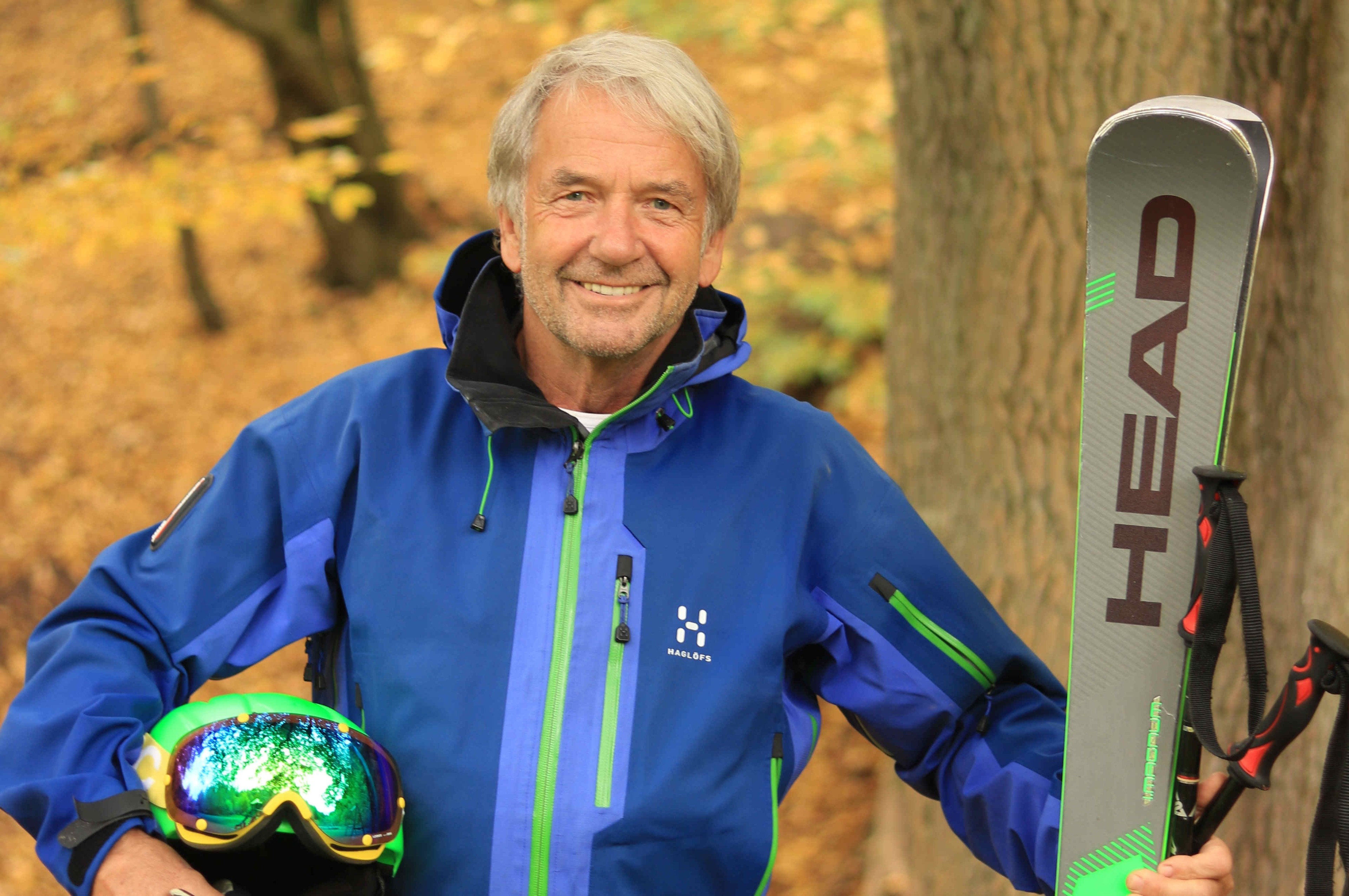 Person in blauer Haglöfs Outdoorjacke mit Skibrille und Ski im herbstlichen Wald