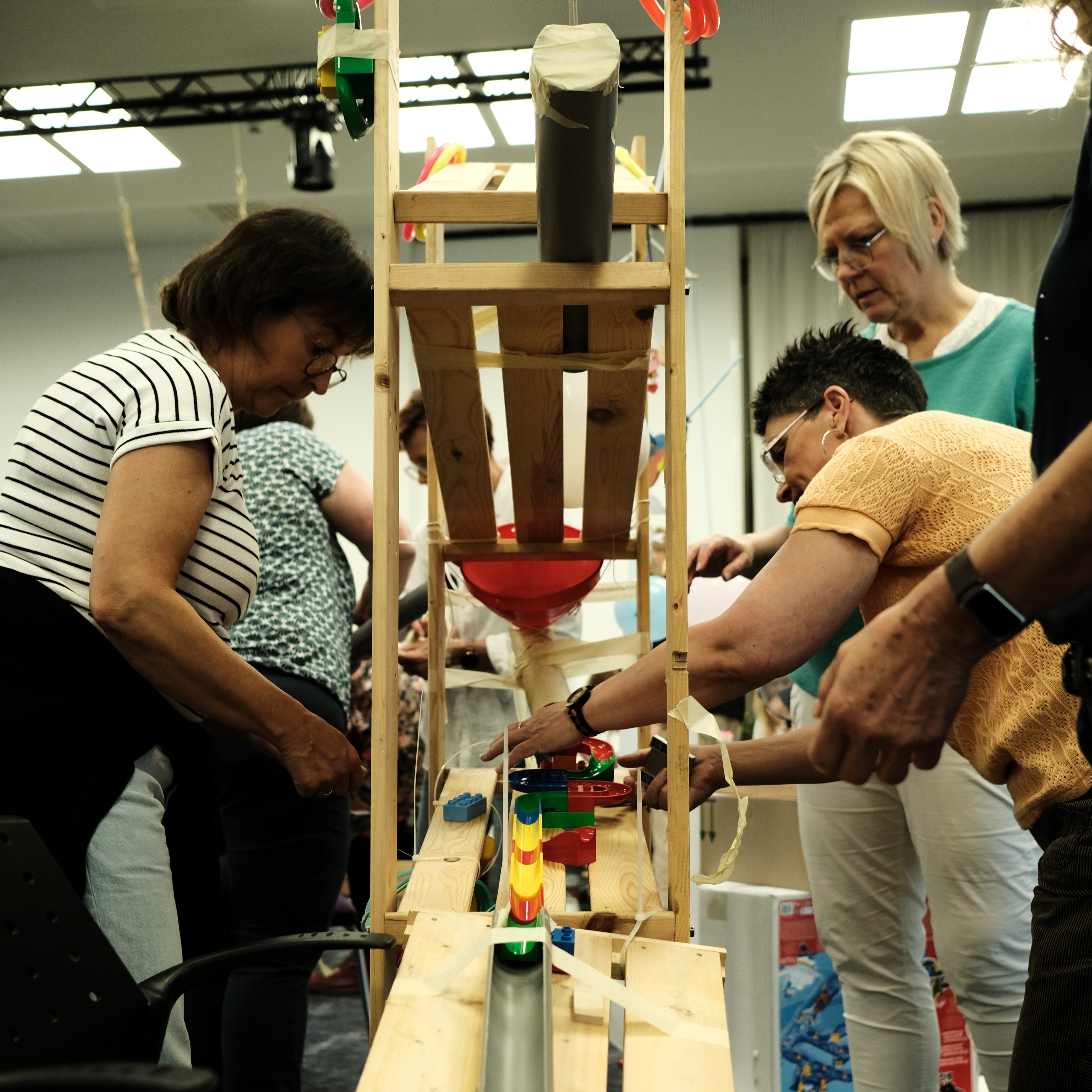 Erwachsene bauen gemeinsam eine kreative Kugelbahn aus Holz und bunten Elementen in einem Veranstaltungsraum