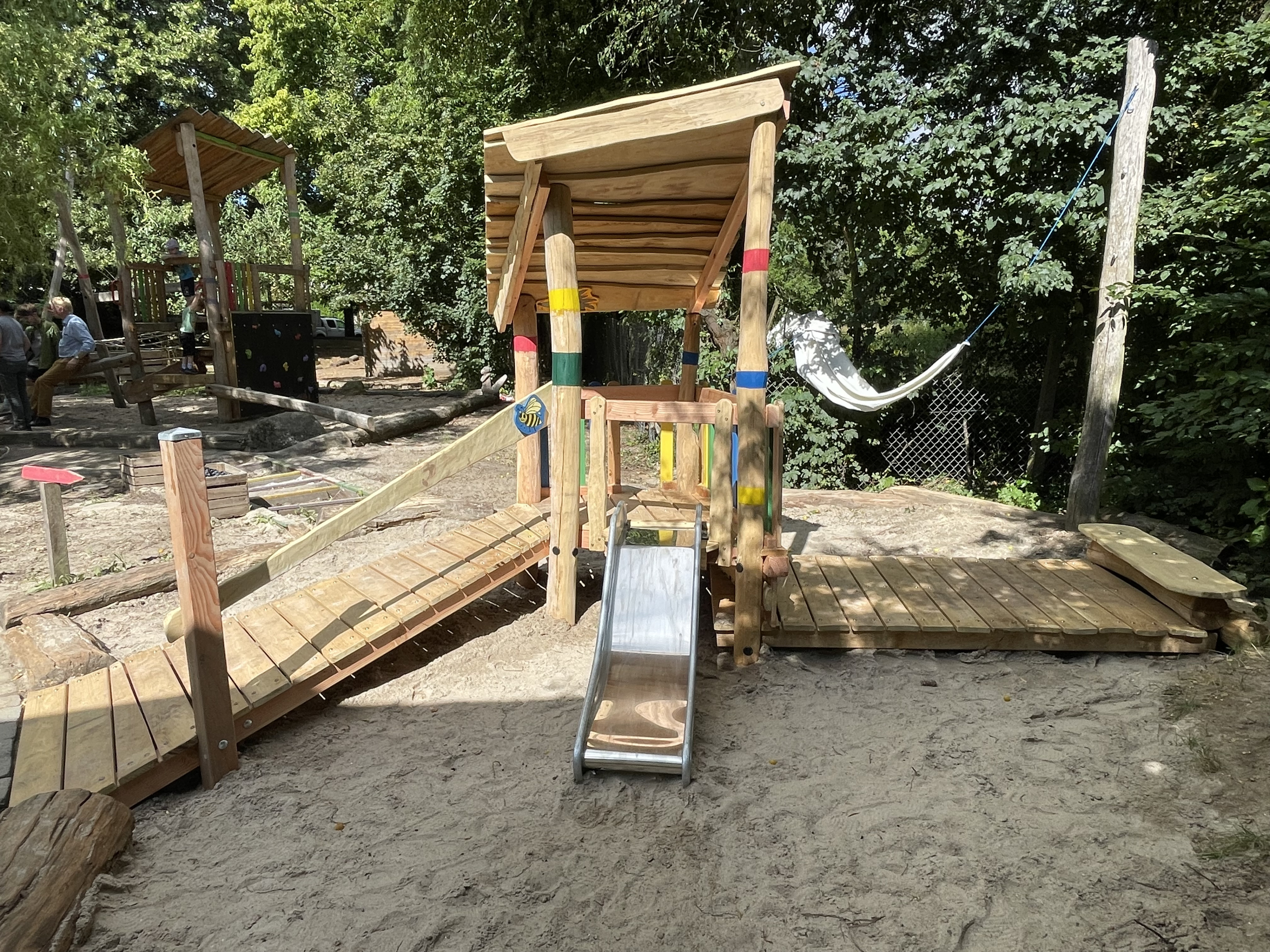 Holzspielplatz mit Rutsche und Hängematte im Freien, umgeben von Bäumen