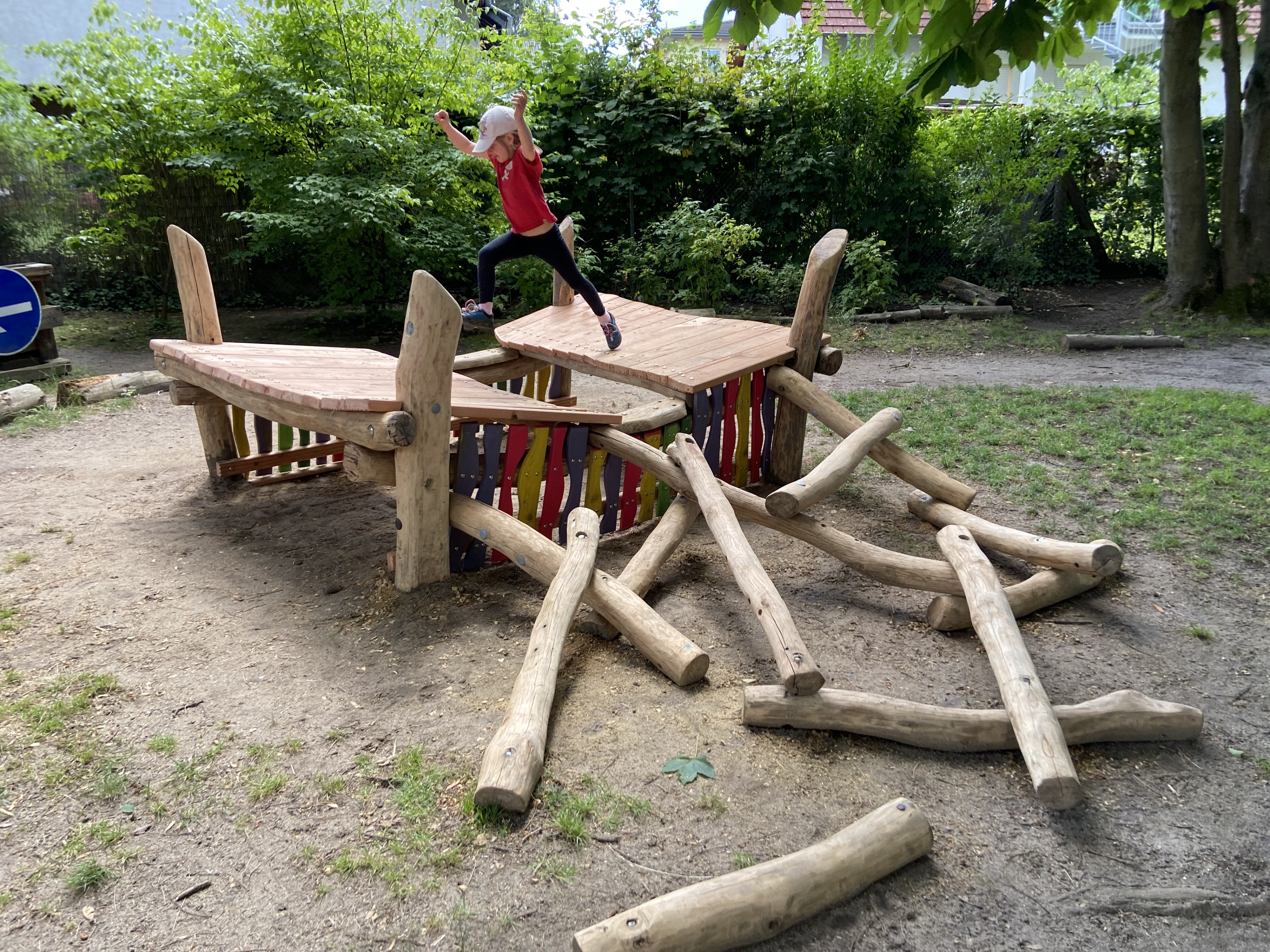 Kind springt auf einem naturnahen Holzspielplatz von einer Plattform zur anderen
