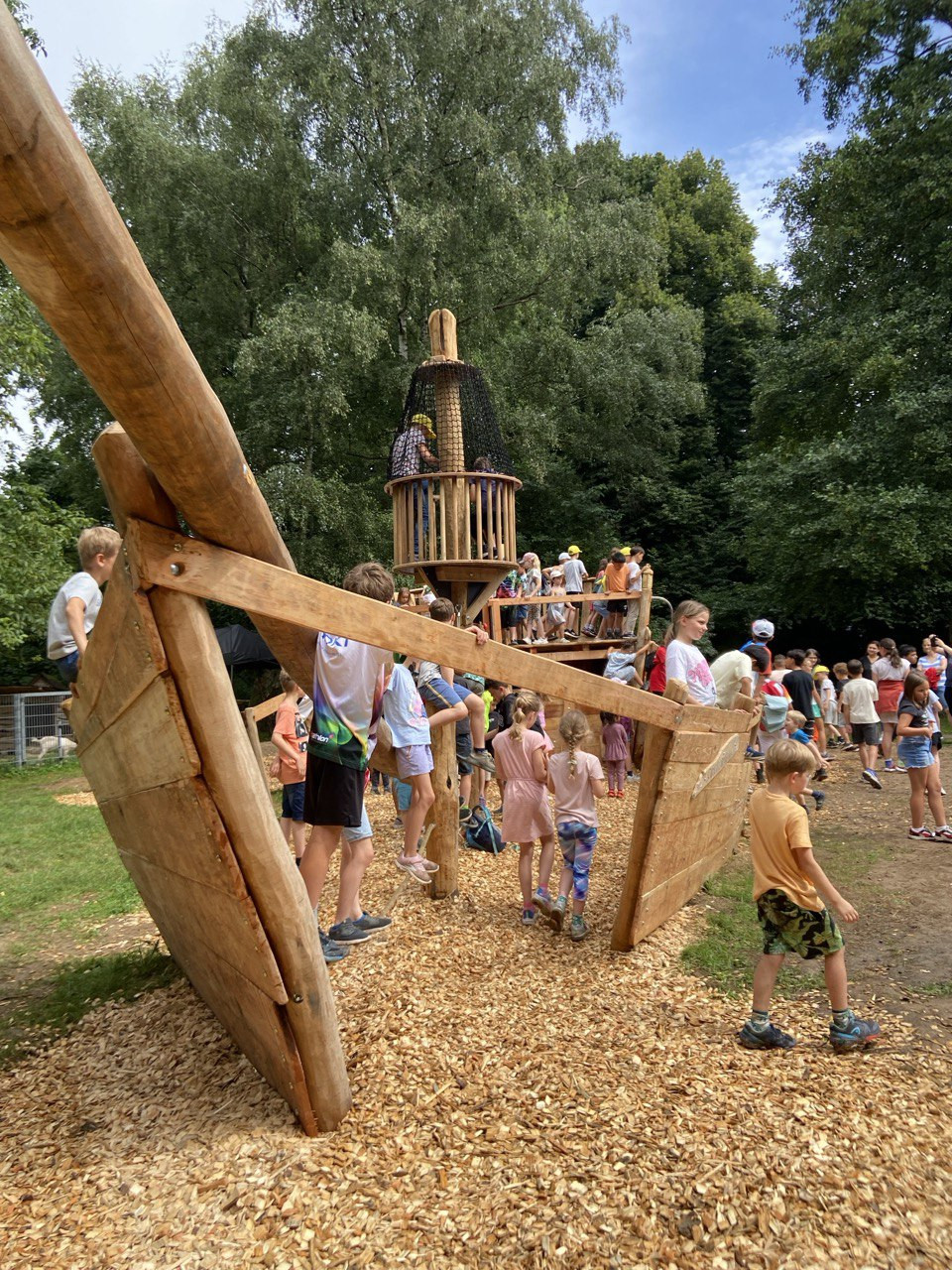 Kinder spielen auf einem großen Holzspielplatz in Form eines Piratenschiffs im Freien