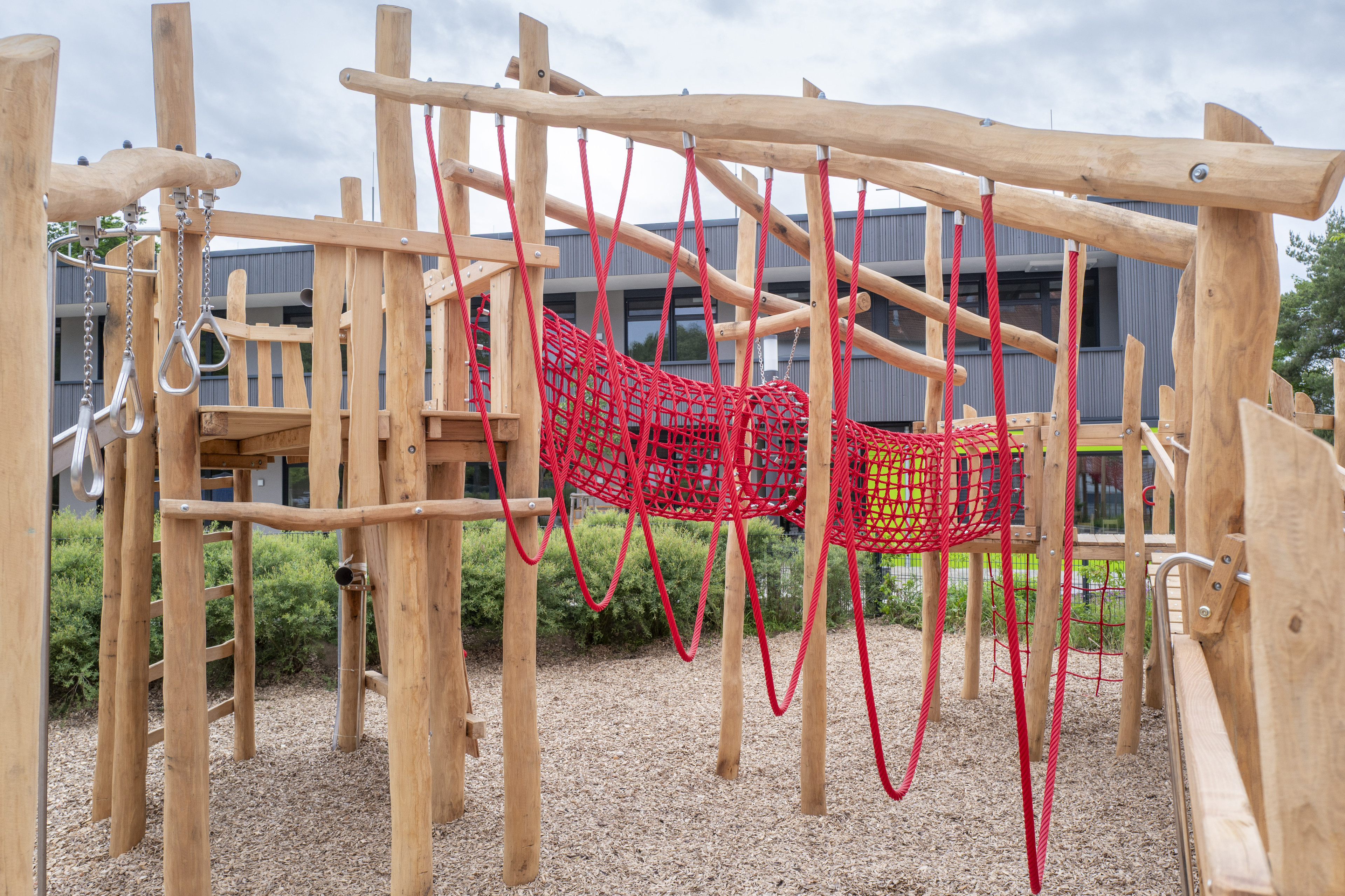 Holzspielplatz mit Klettergerüst und roten Kletternetzen, modernes Außengelände