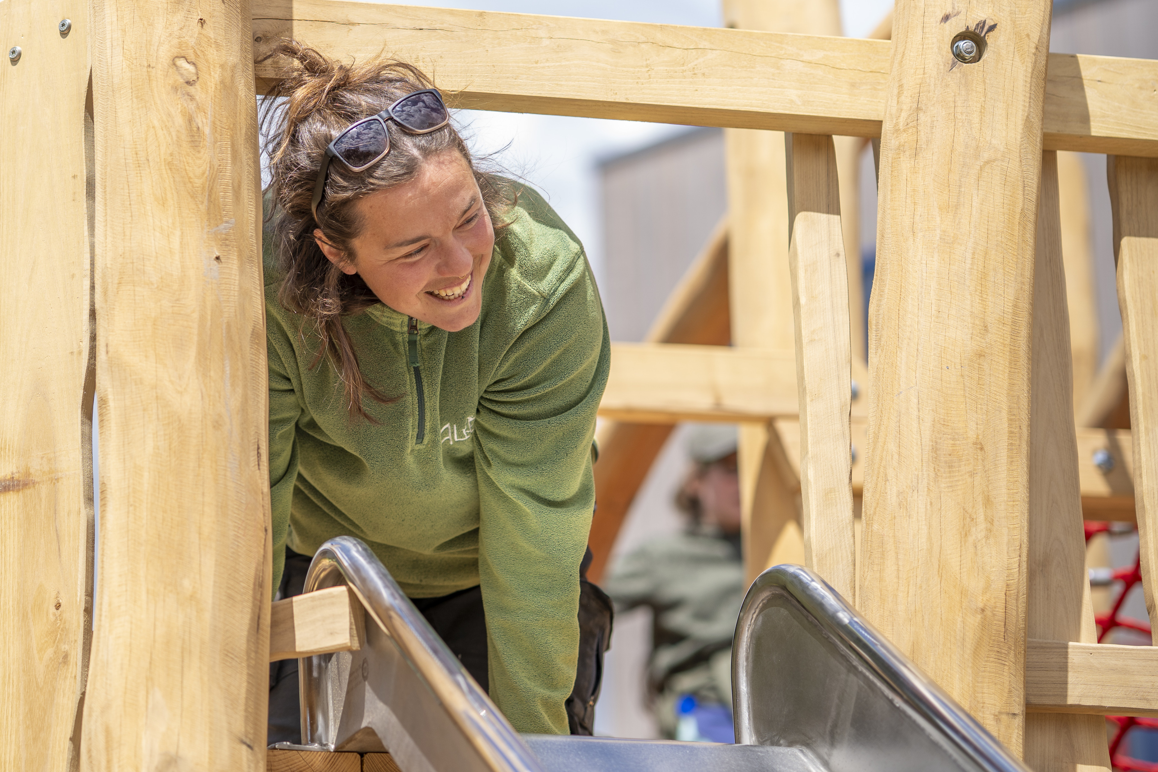 Person mit grünem Pullover auf Holzspielplatz an einer Rutsche