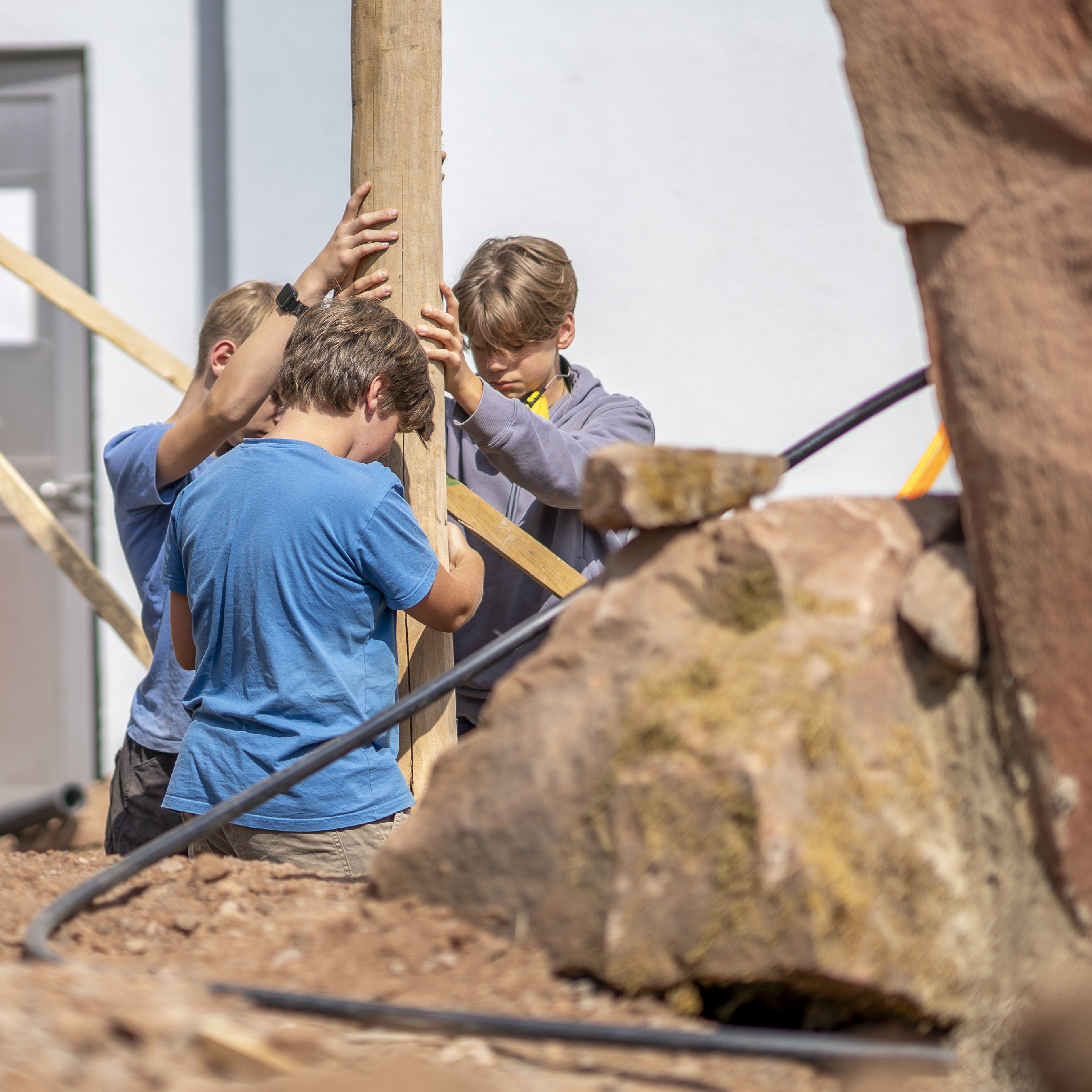 Jugendliche arbeiten gemeinsam an einem Bauprojekt und richten einen Holzpfosten aus