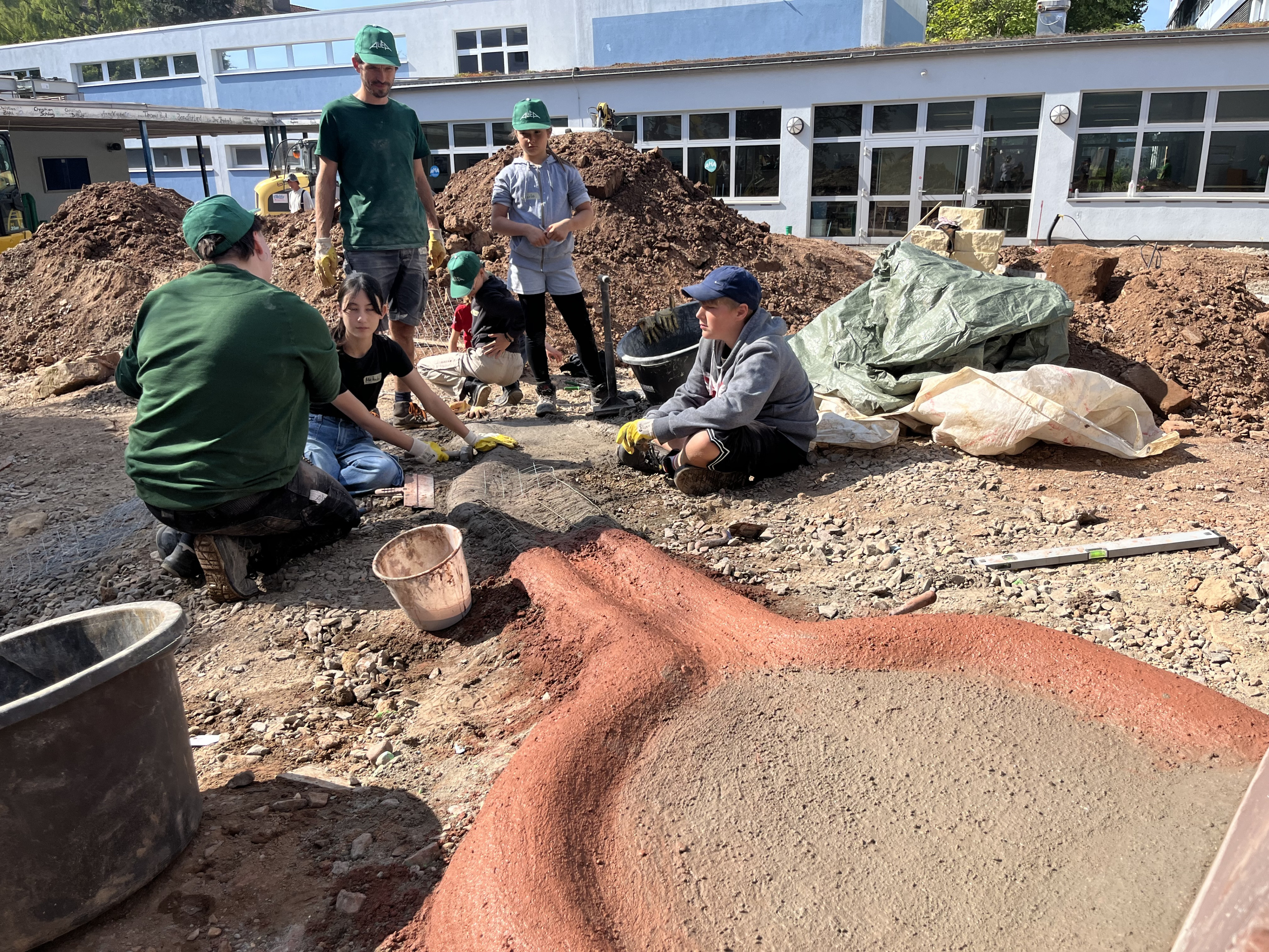 Kinder und Erwachsene arbeiten gemeinsam auf einer Baustelle im Freien vor einem Schulgebäude