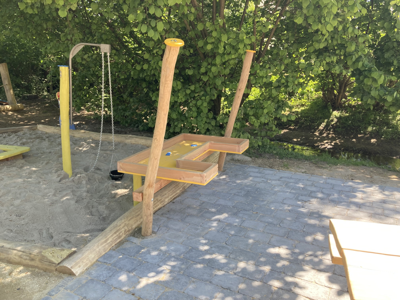 Moderner Wasserspielplatz mit Holz-Wasserbahn und Sandbereich im Freien