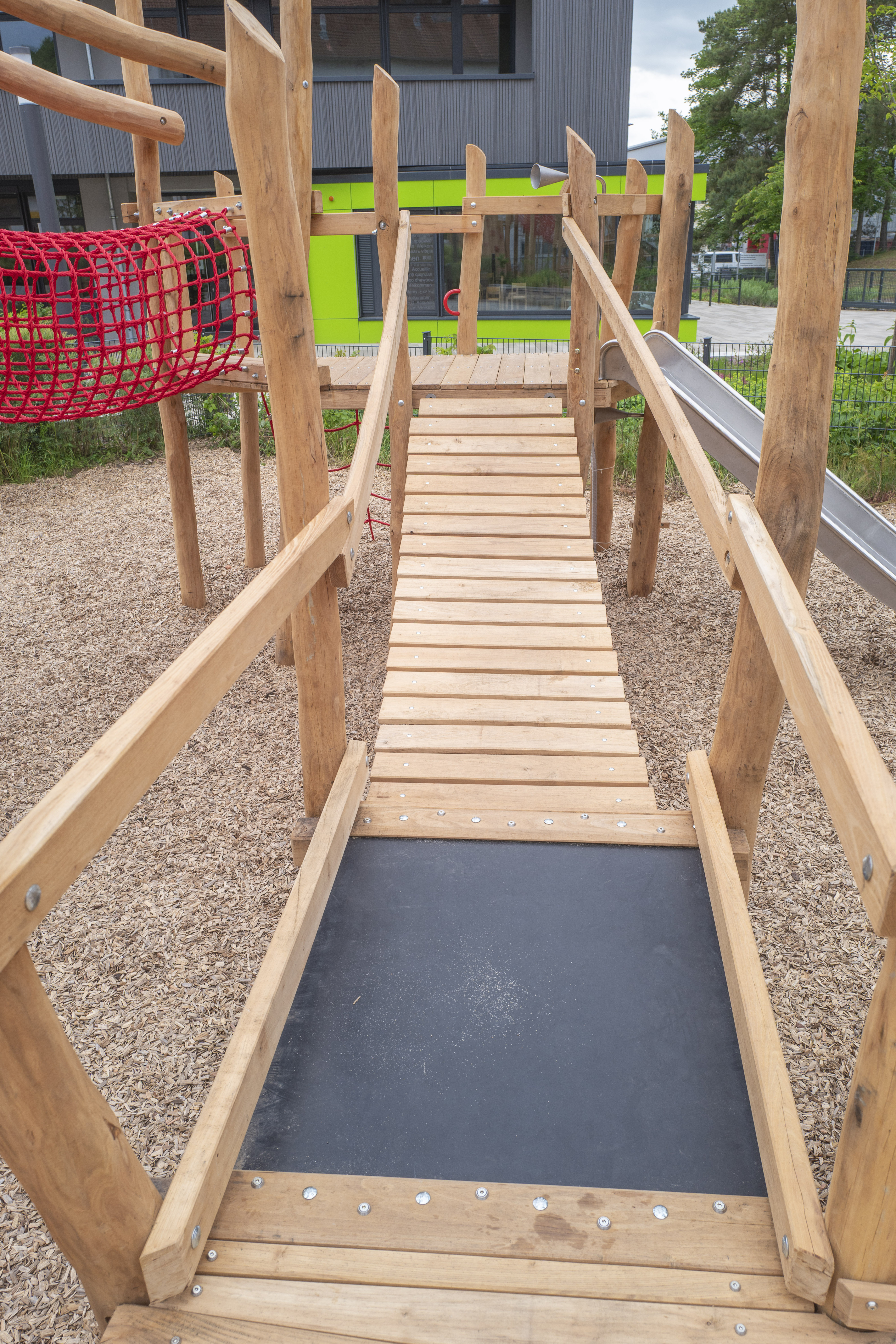 Holzbrücke auf einem modernen Spielplatz mit Kletterelementen und Rutsche