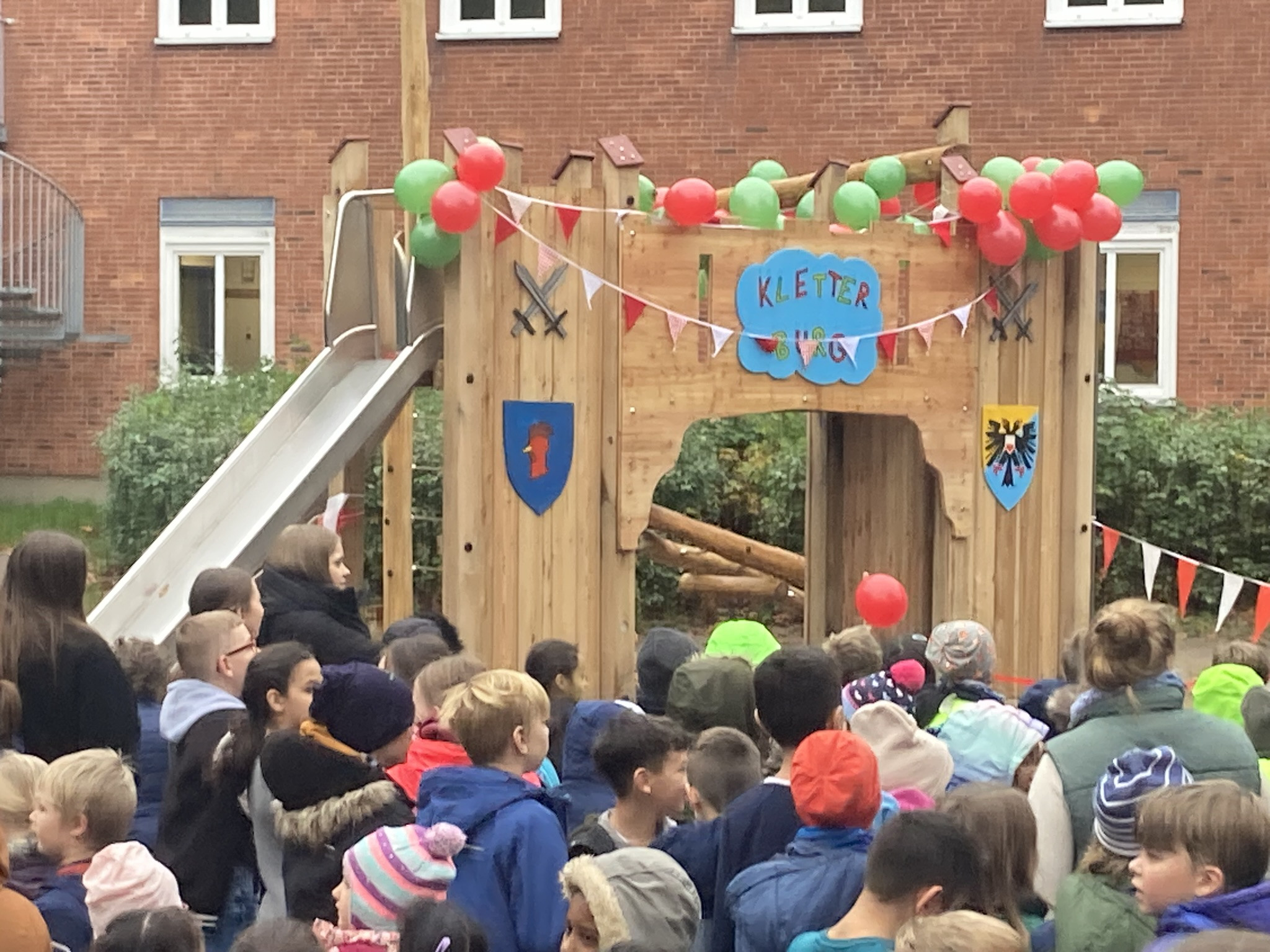 Eröffnung eines neuen Kletterturms mit Rutsche und vielen Kindern auf einem Schulhof