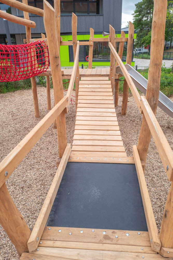 Holzbrücke auf einem modernen Spielplatz mit Kletternetz und Rutsche
