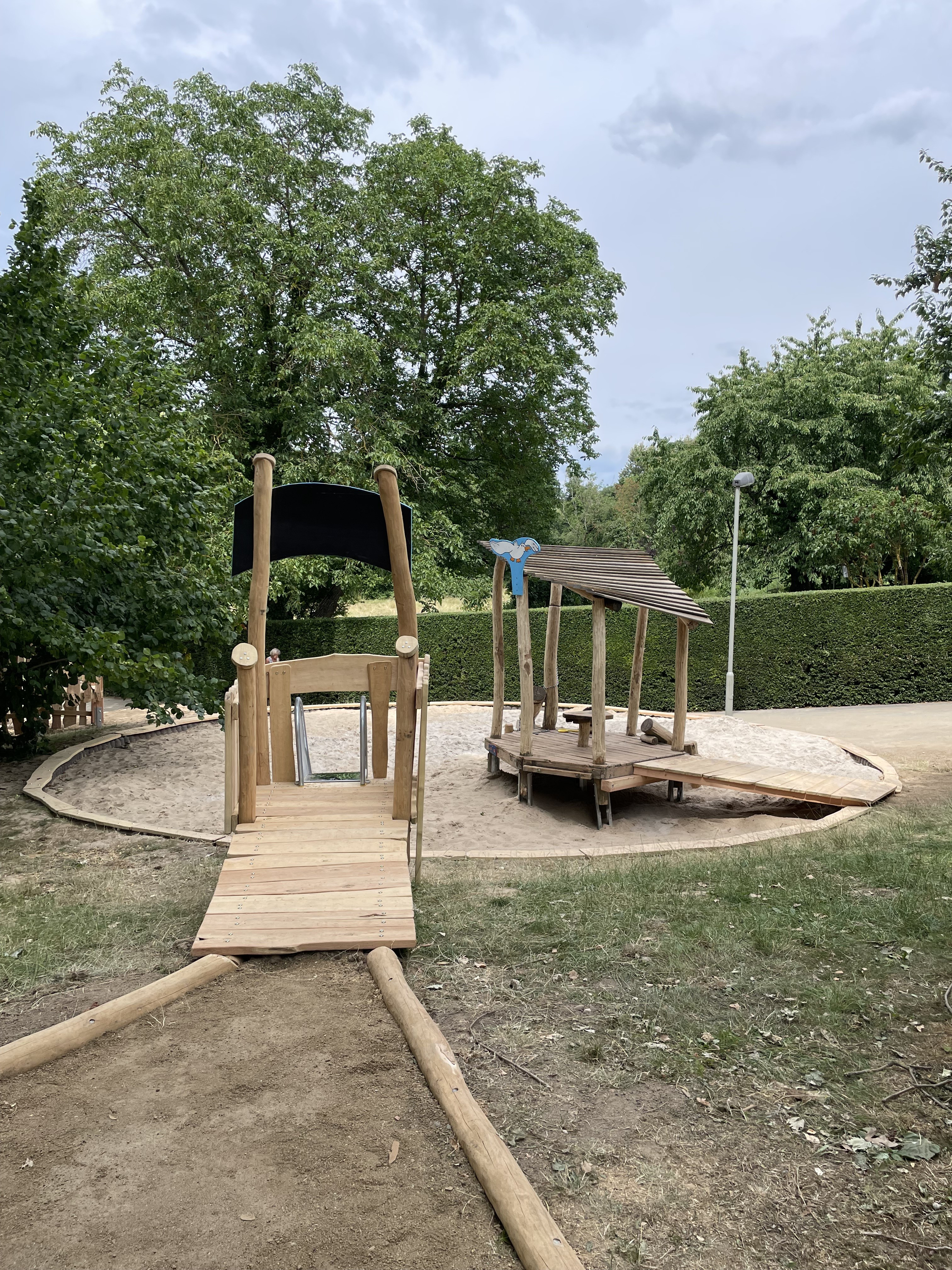 Moderner Spielplatz mit Holzspielgeräten und Sandfläche im Grünen