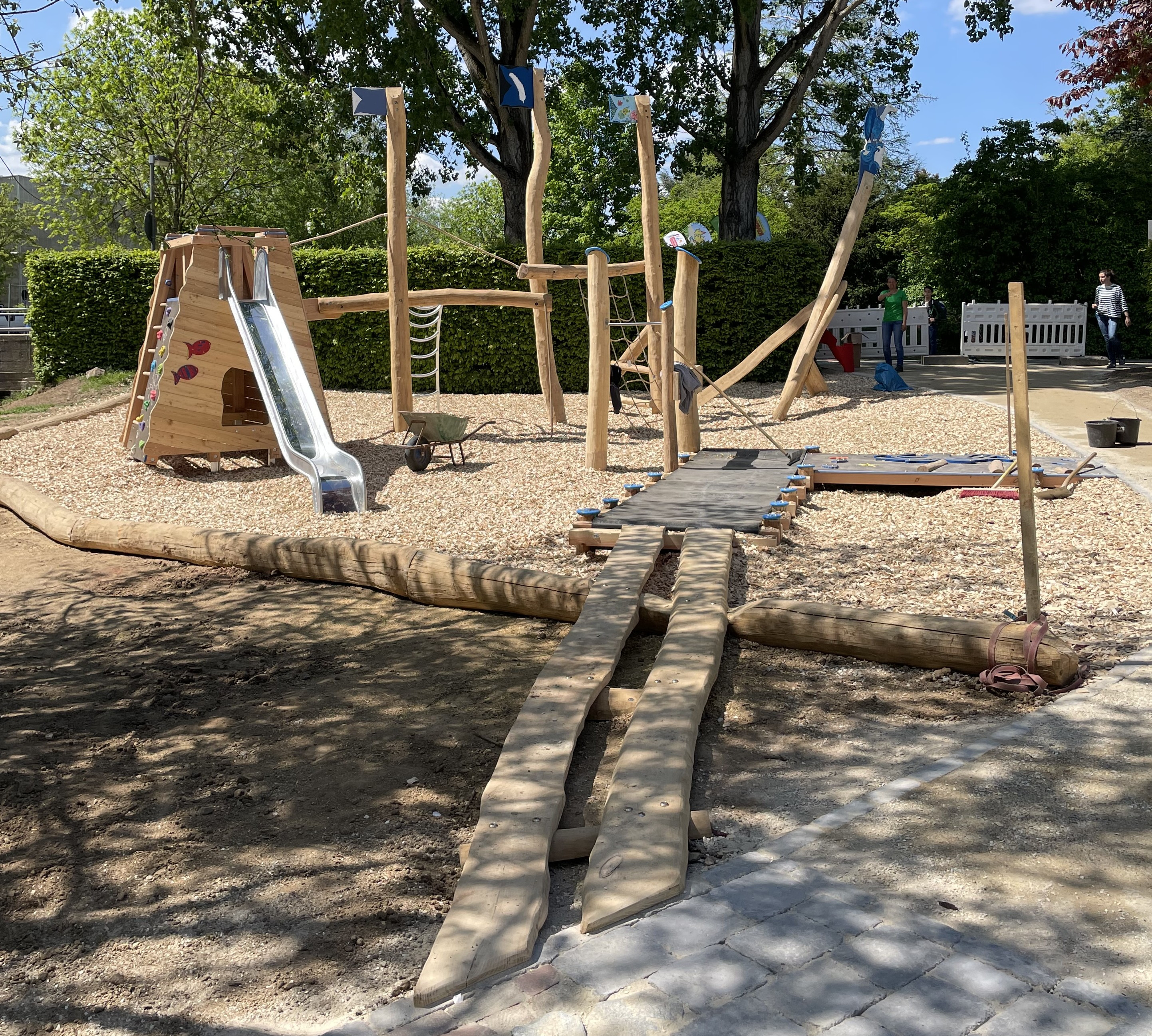 Moderner Holzspielplatz mit Rutsche, Kletterelementen und Balancierbrücke an einem sonnigen Tag