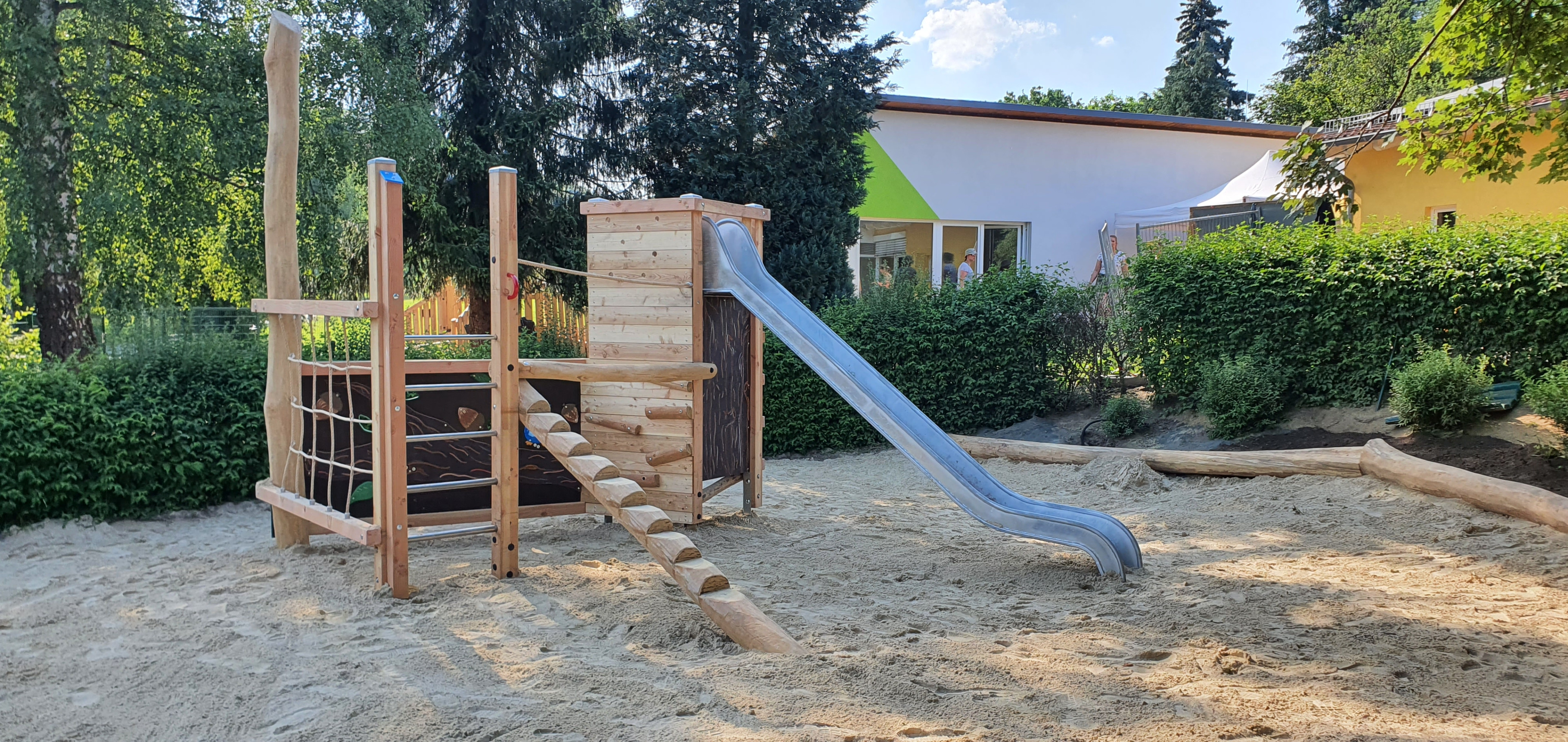 Moderner Spielplatz mit Holz-Klettergerüst und Rutsche auf Sandfläche im Freien
