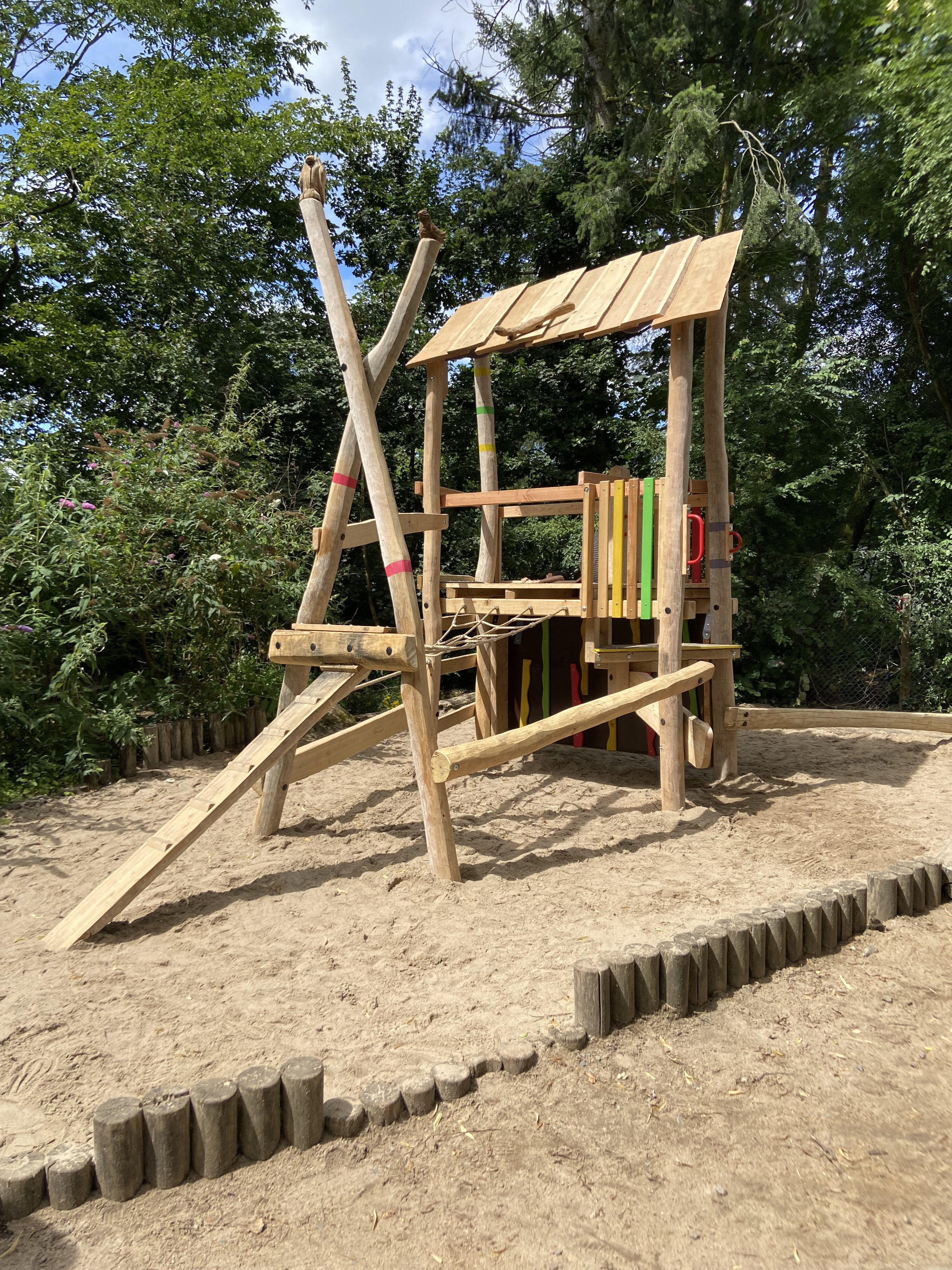 Holzspielplatz mit Klettergerüst und Rutsche im Sandbereich