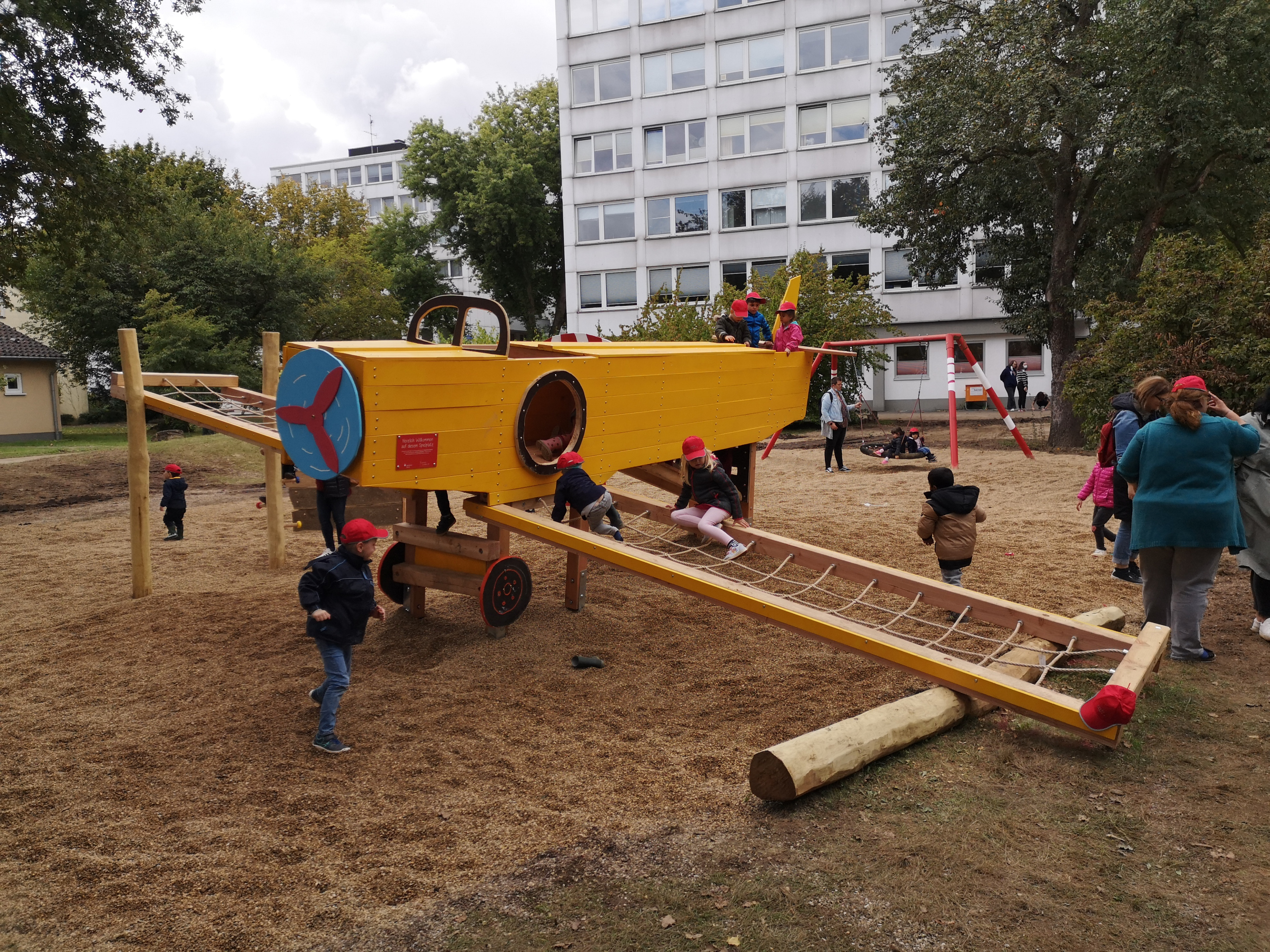 Kinder spielen auf einem Spielplatz mit gelbem Flugzeug-Klettergerüst vor einem Wohnhaus