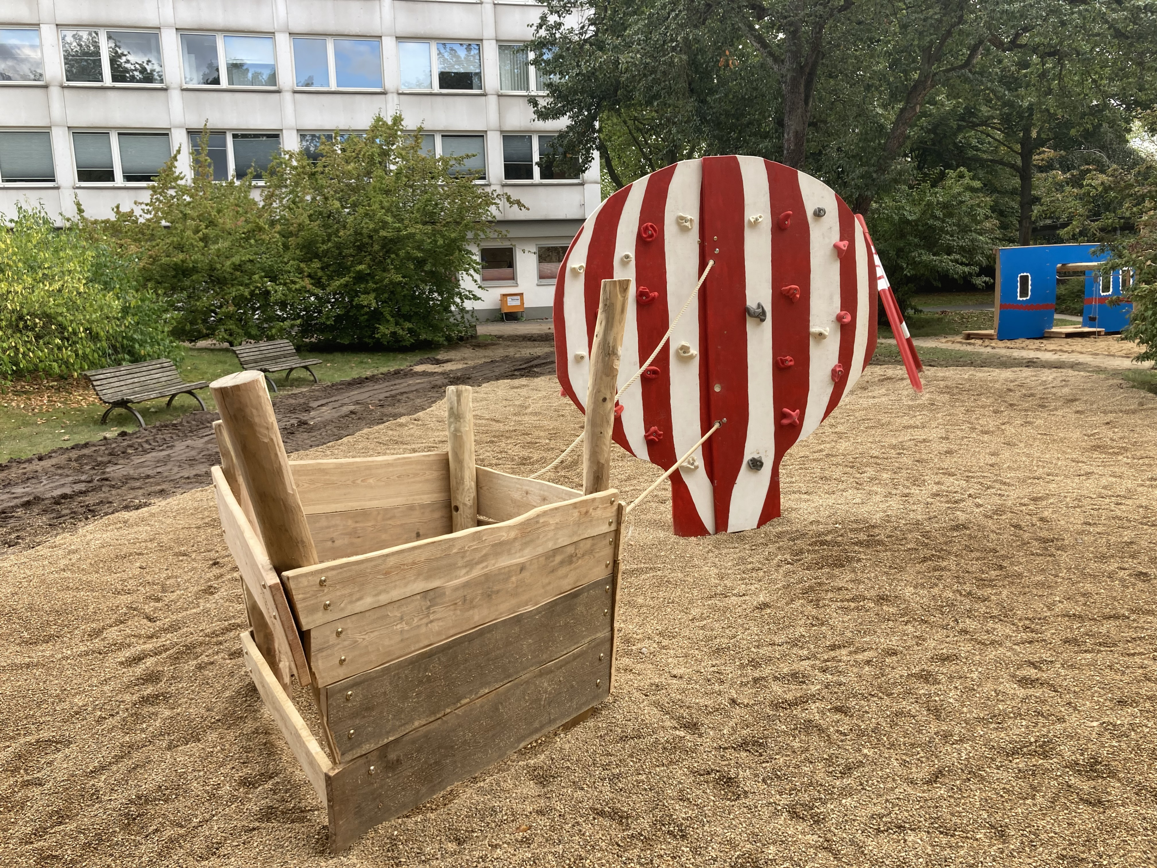 Spielplatz mit Heißluftballon-Klettergerüst aus Holz und Sandfläche vor Wohnhaus