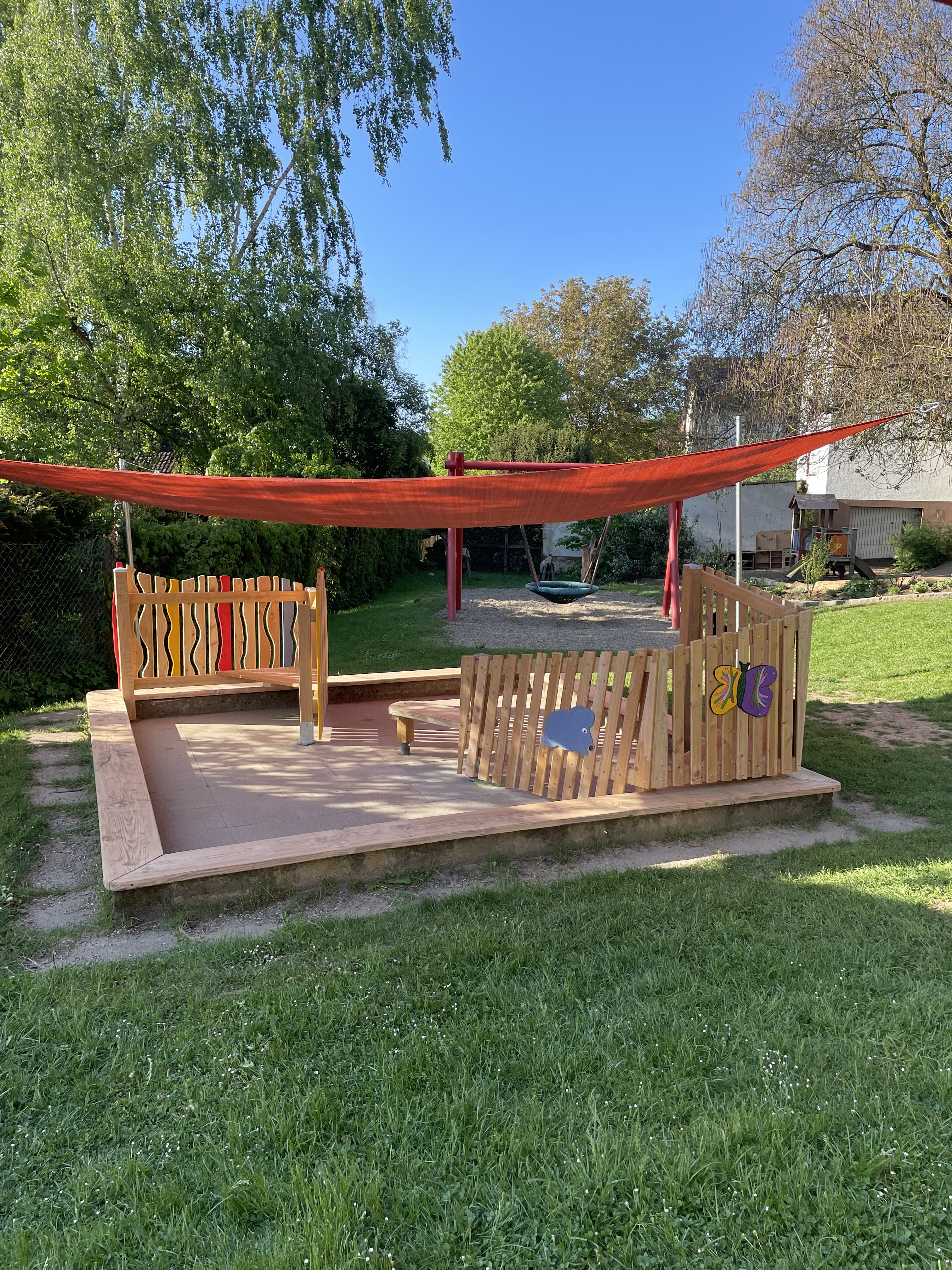 Moderner Sandkasten mit Holzumrandung und Sonnensegel auf einem Spielplatz im Grünen