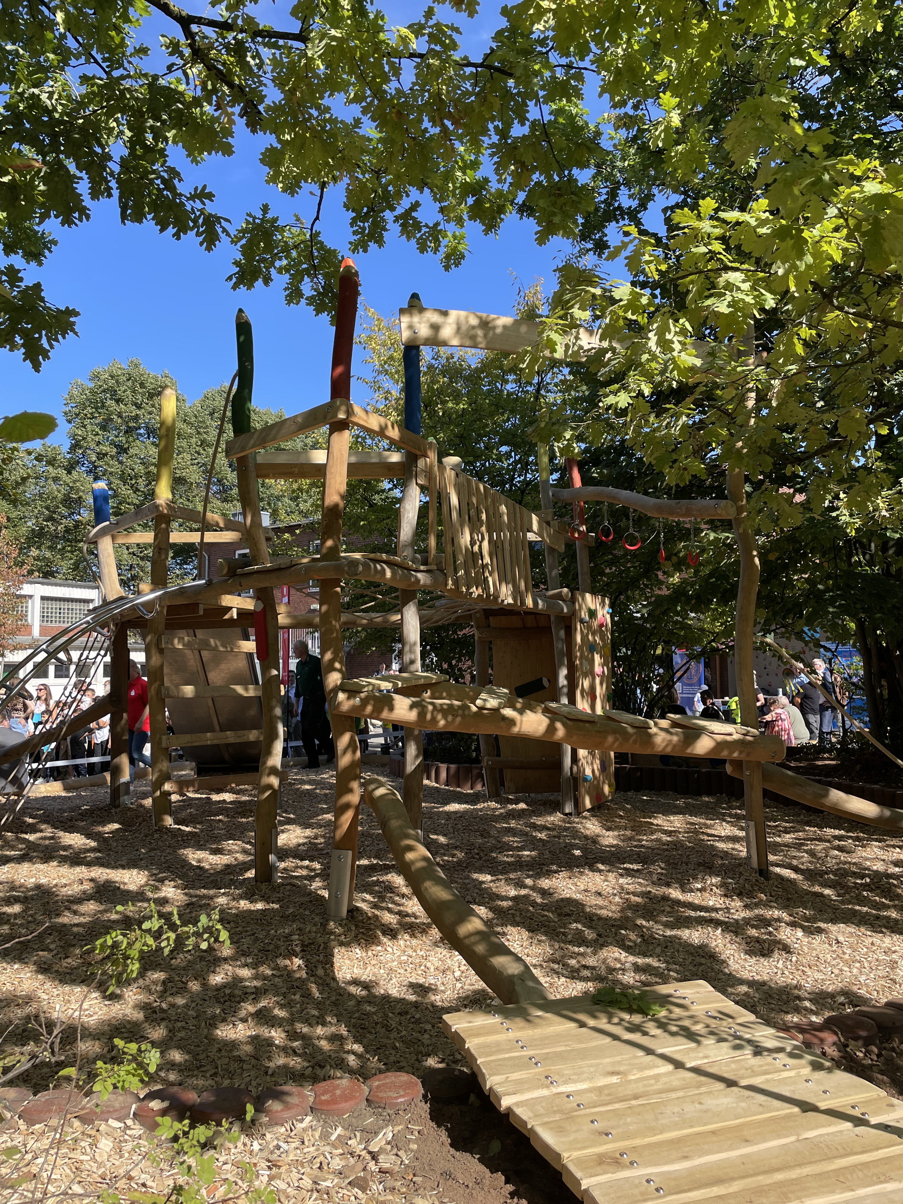 Abenteuerspielplatz aus Holz mit Klettergerüst und Rutschen im Freien bei sonnigem Wetter