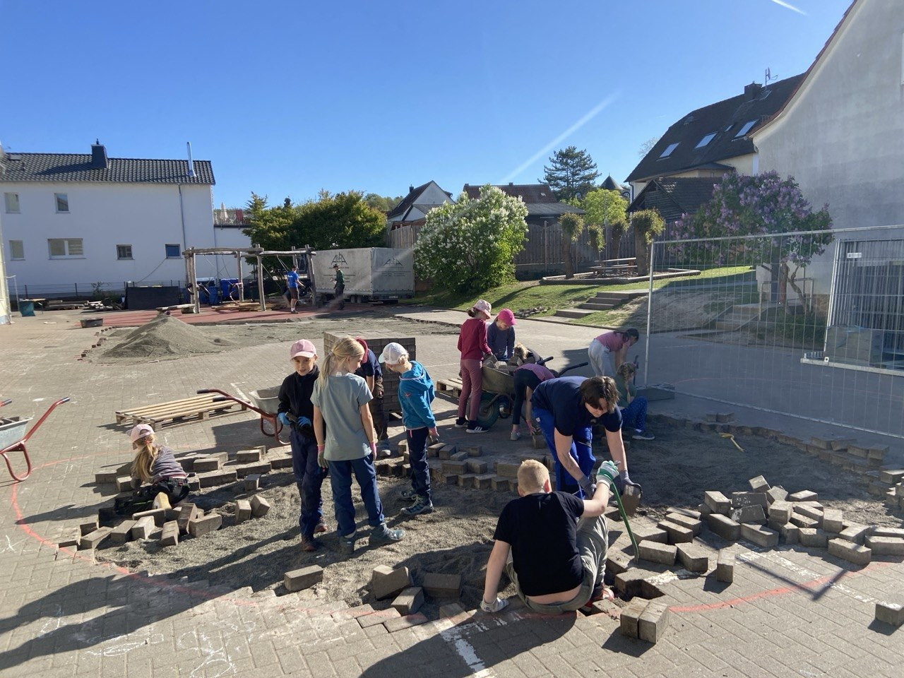 Kinder helfen beim Bau eines Schulhofs und verlegen Pflastersteine bei sonnigem Wetter