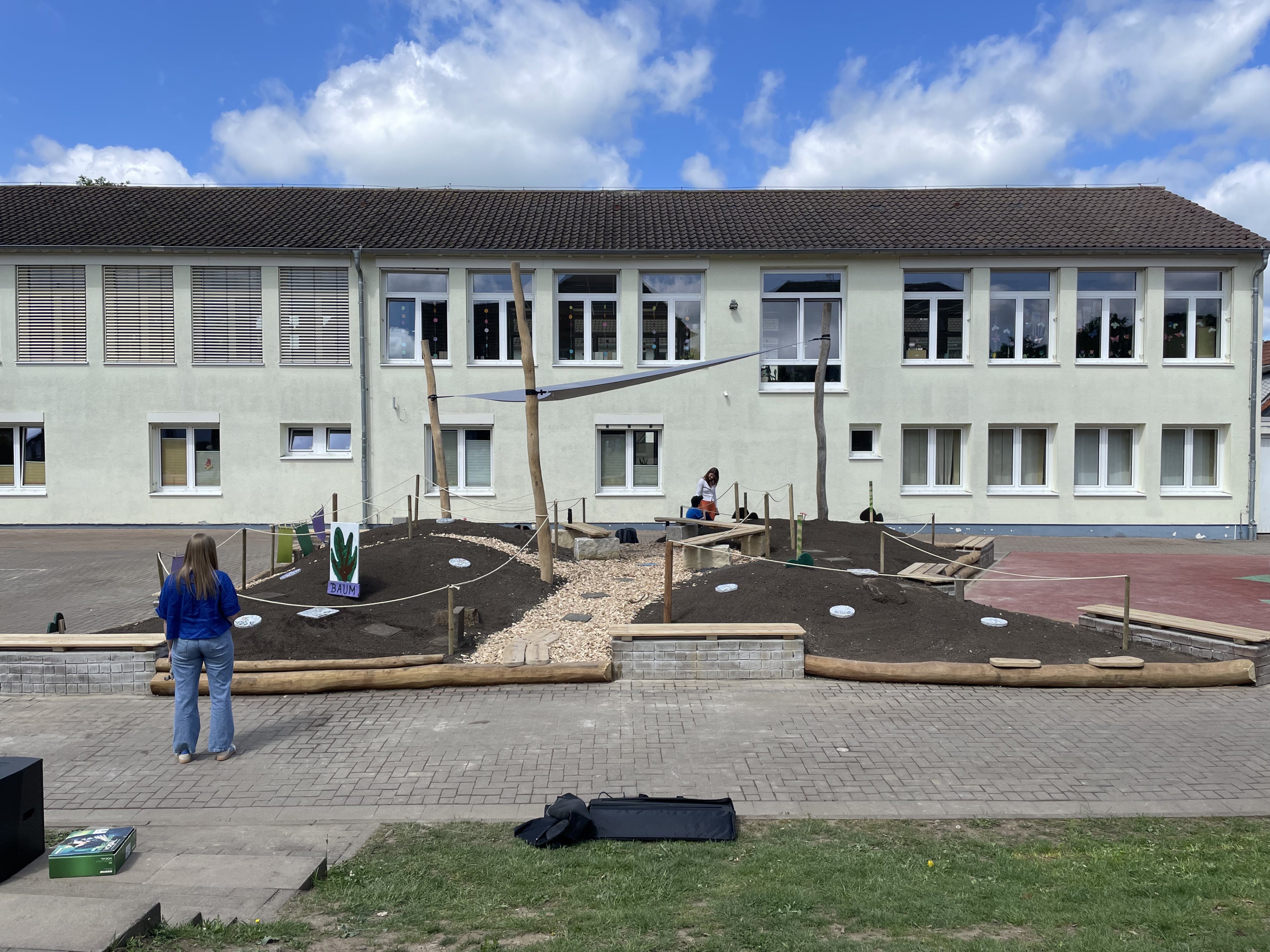 Schulhof mit neu angelegtem Schulgarten und Spielbereich vor einem Schulgebäude