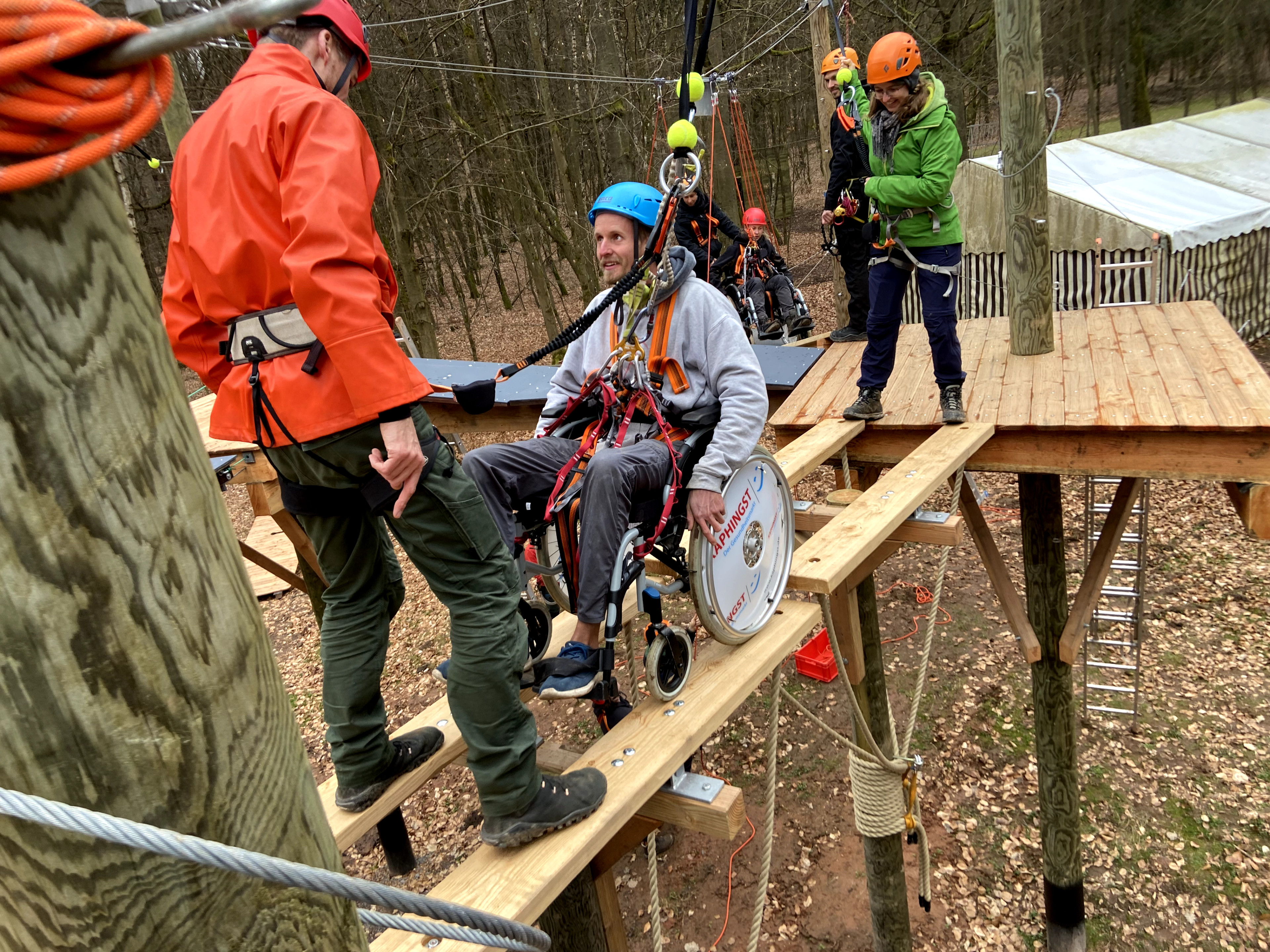 Barrierefreier Hochseilgarten: Rollstuhlfahrer mit Begleitern auf Holzplattform im Wald