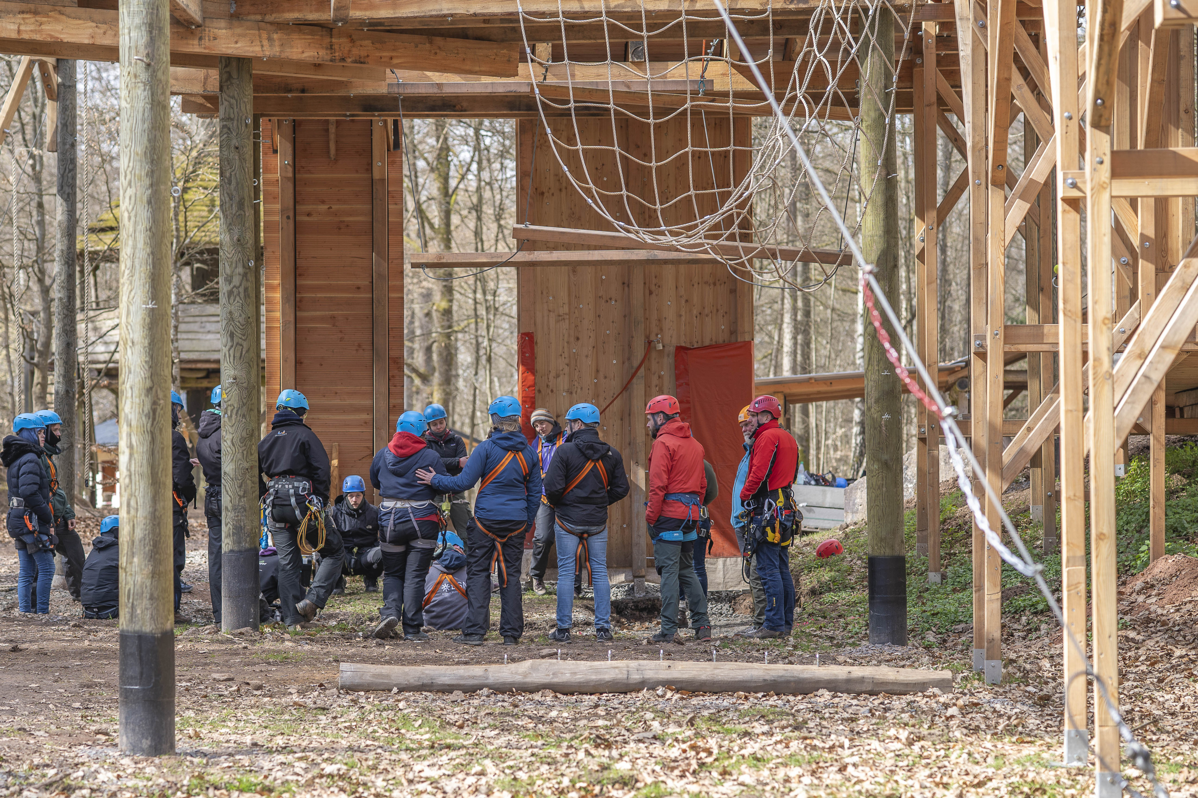 Gruppe von Menschen mit Helmen und Kletterausrüstung bei einer Teambuilding-Aktivität im Hochseilgarten