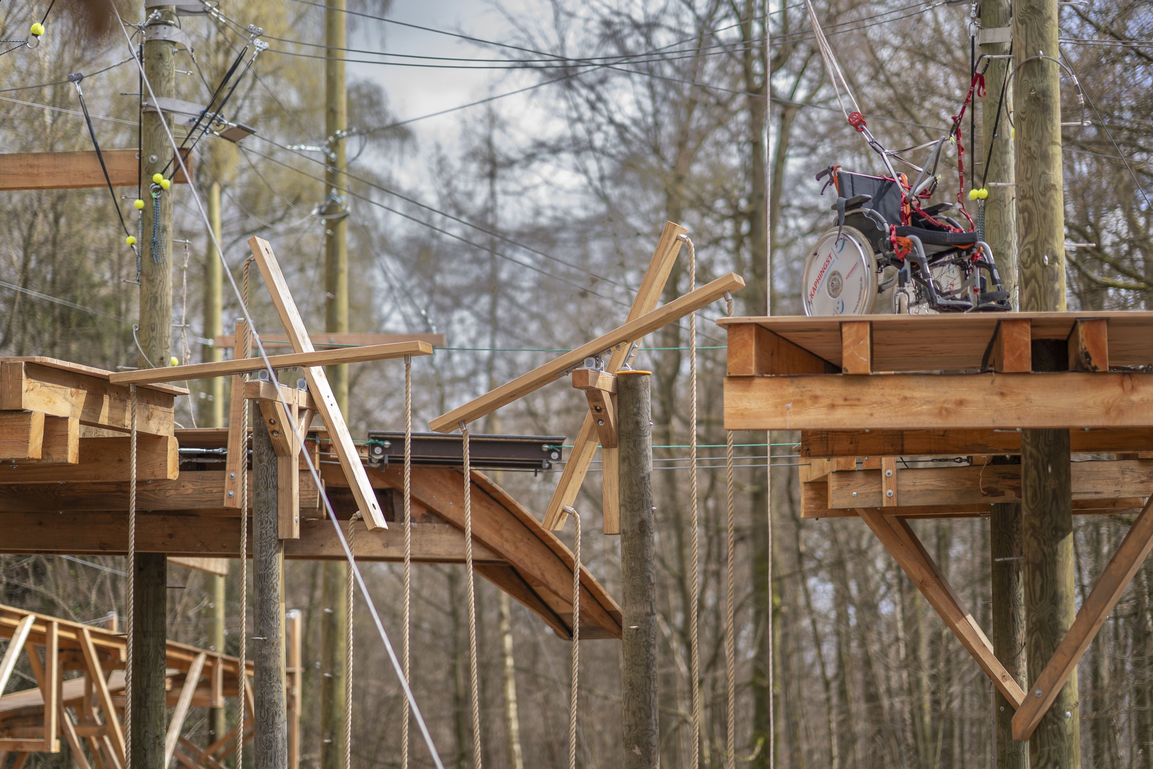 Barrierefreier Hochseilgarten mit Rollstuhlzugang, Holzplattformen und Seilbahn im Wald