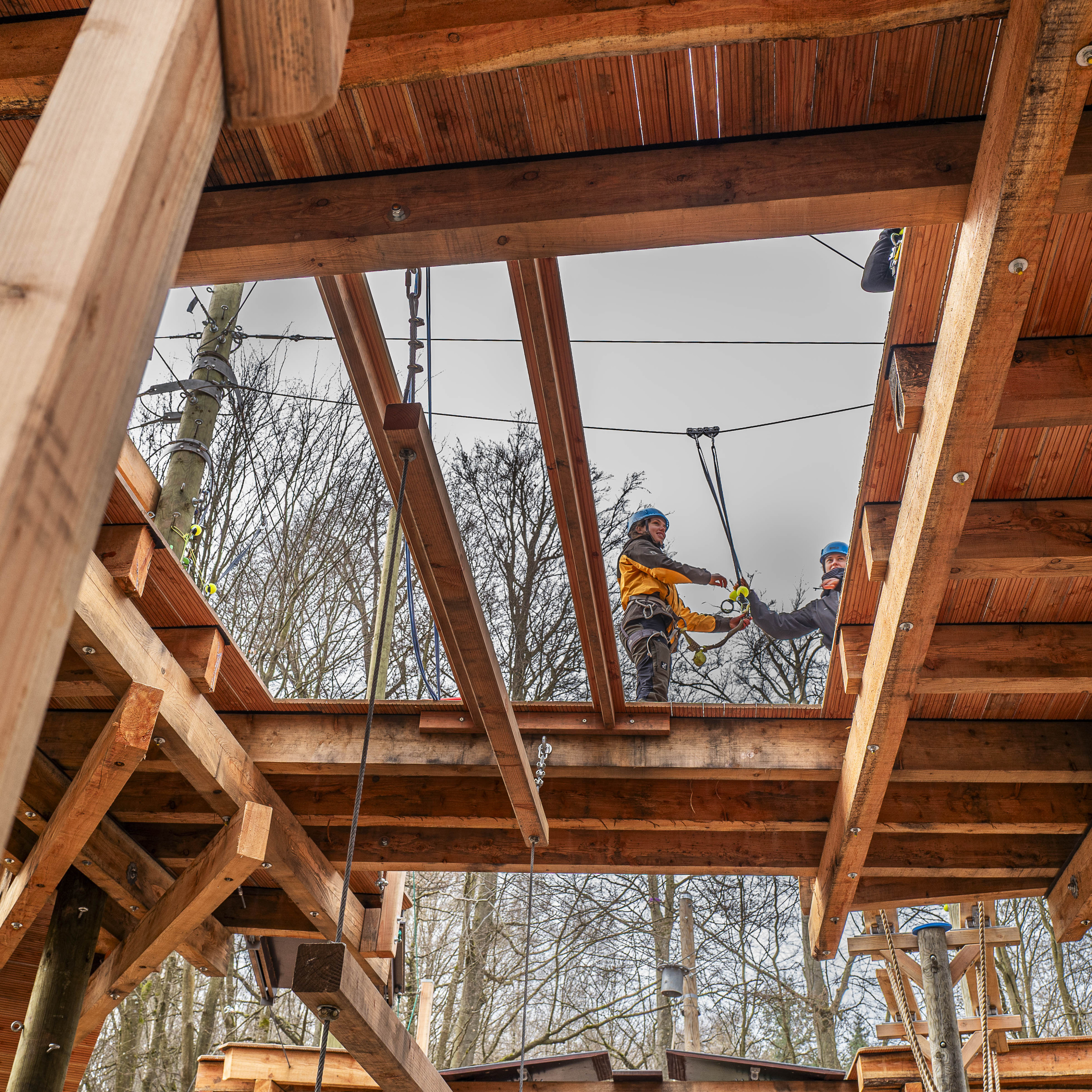 Zwei Personen mit Helmen beim Klettern im Hochseilgarten auf einer Holzkonstruktion