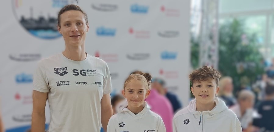 Drei Mitglieder eines Schwimmteams vor einer Pressewand bei einem Sportevent