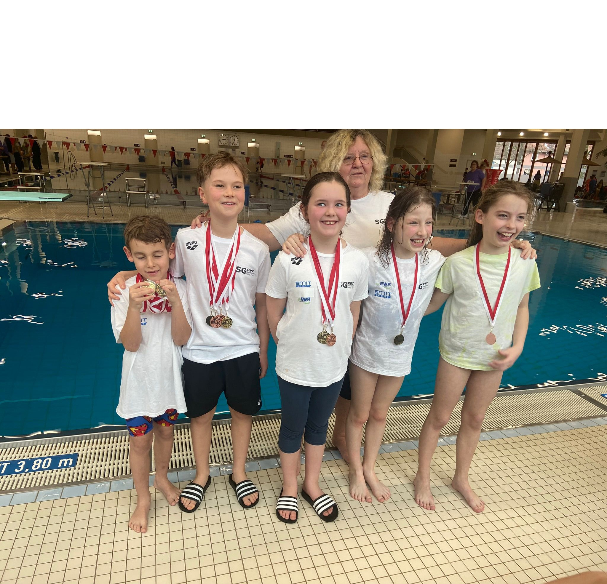 Kinder mit Medaillen bei einem Schwimmwettkampf am Beckenrand