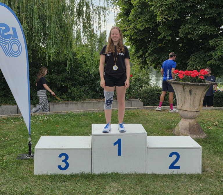 Sportlerin auf dem Siegerpodest mit Medaille beim Sportevent im Freien Sportlerin mit Medaille steht auf dem ersten Platz eines Siegerpodests im Freien