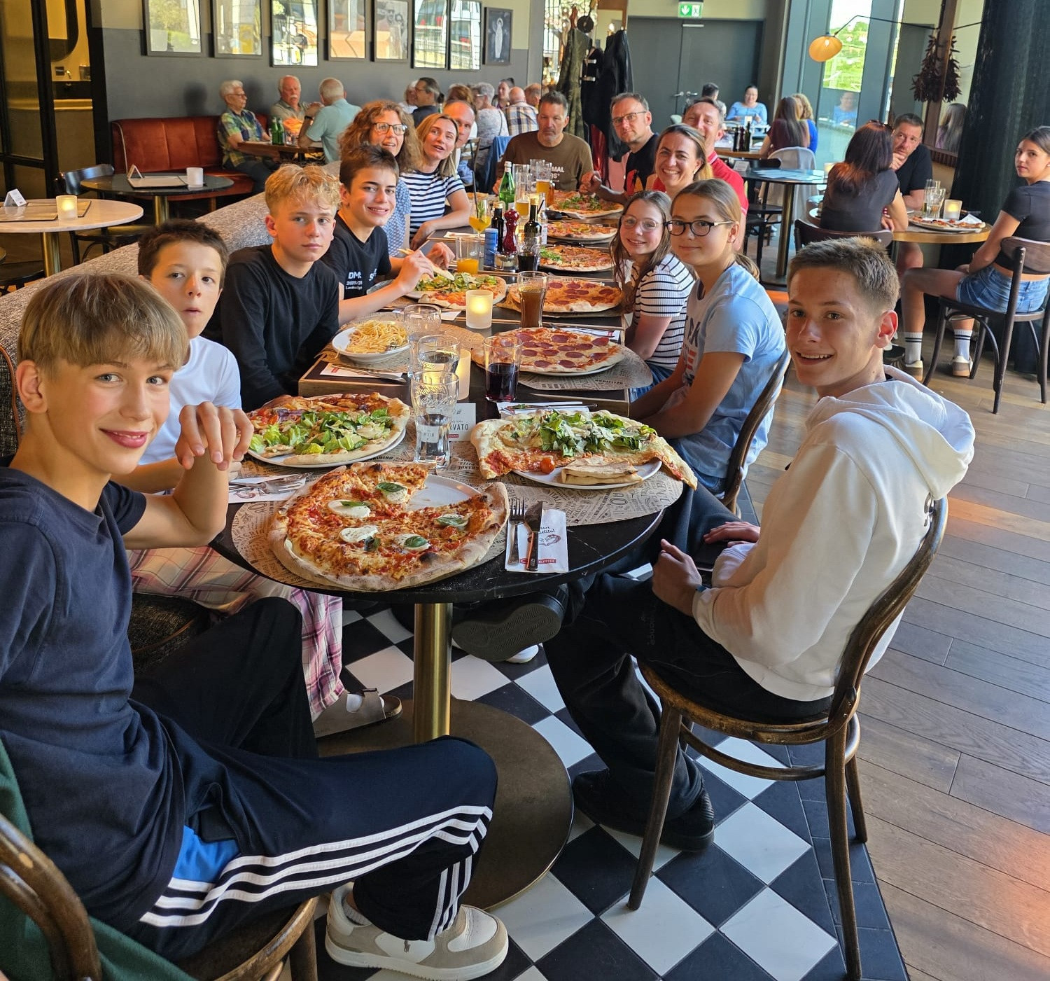 Gruppe von Jugendlichen isst gemeinsam Pizza in einem modernen Restaurant, große Pizzen auf dem Tisch