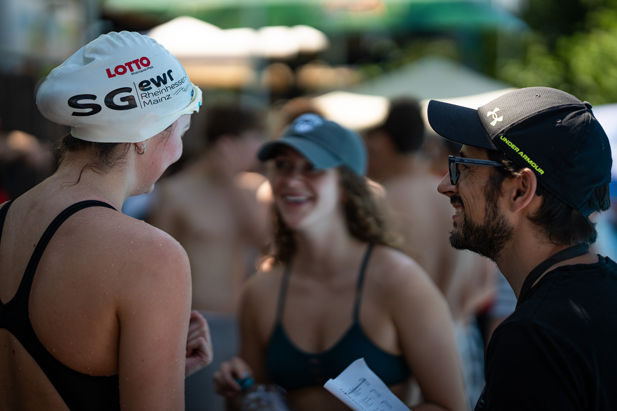 Schwimmerin mit Badekappe des Vereins Rheinhessen Mainz im Gespräch mit Teammitgliedern am Beckenrand