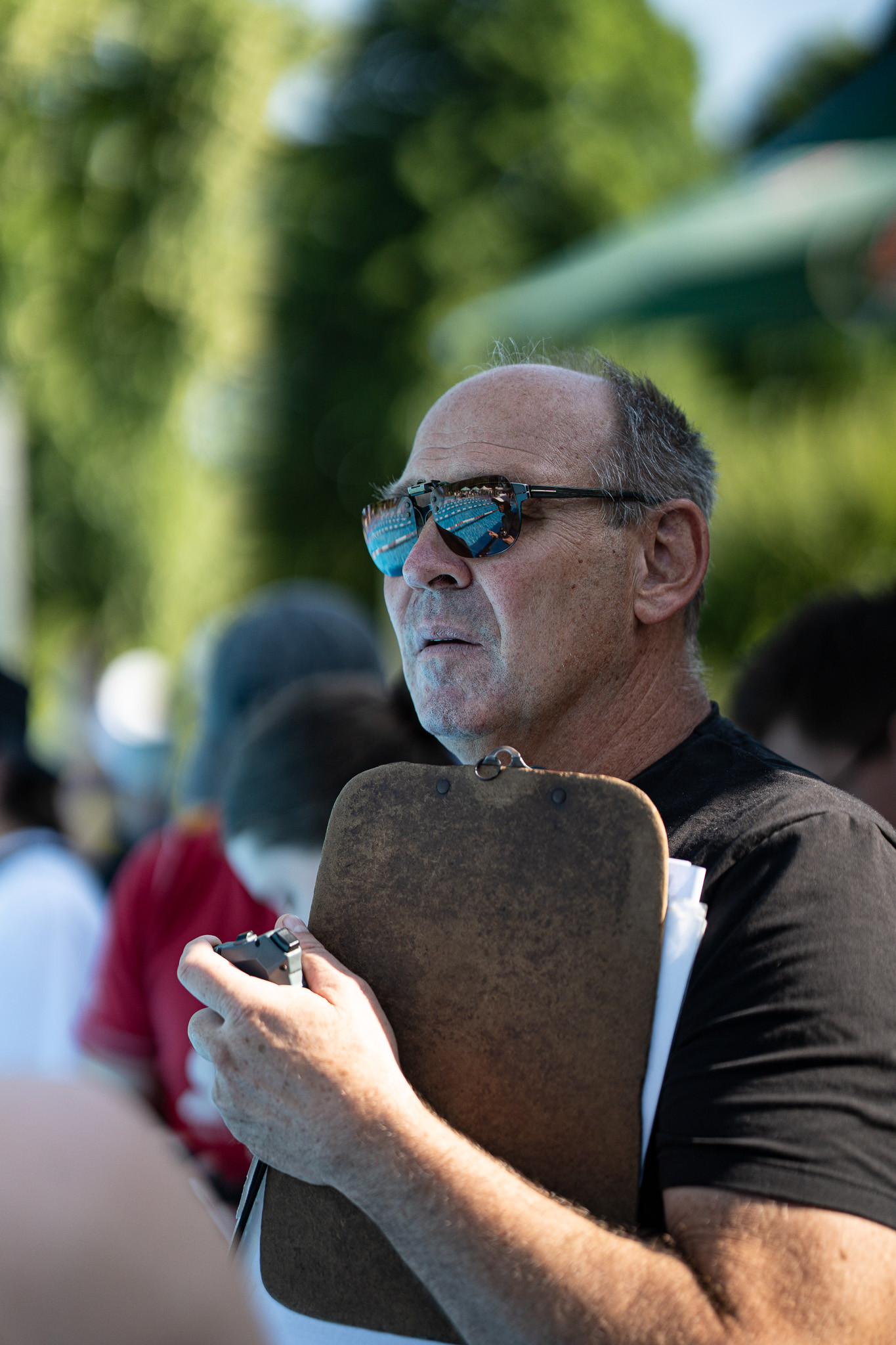 Mann mit Sonnenbrille und Klemmbrett beobachtet ein Schwimmwettkampf im Freien