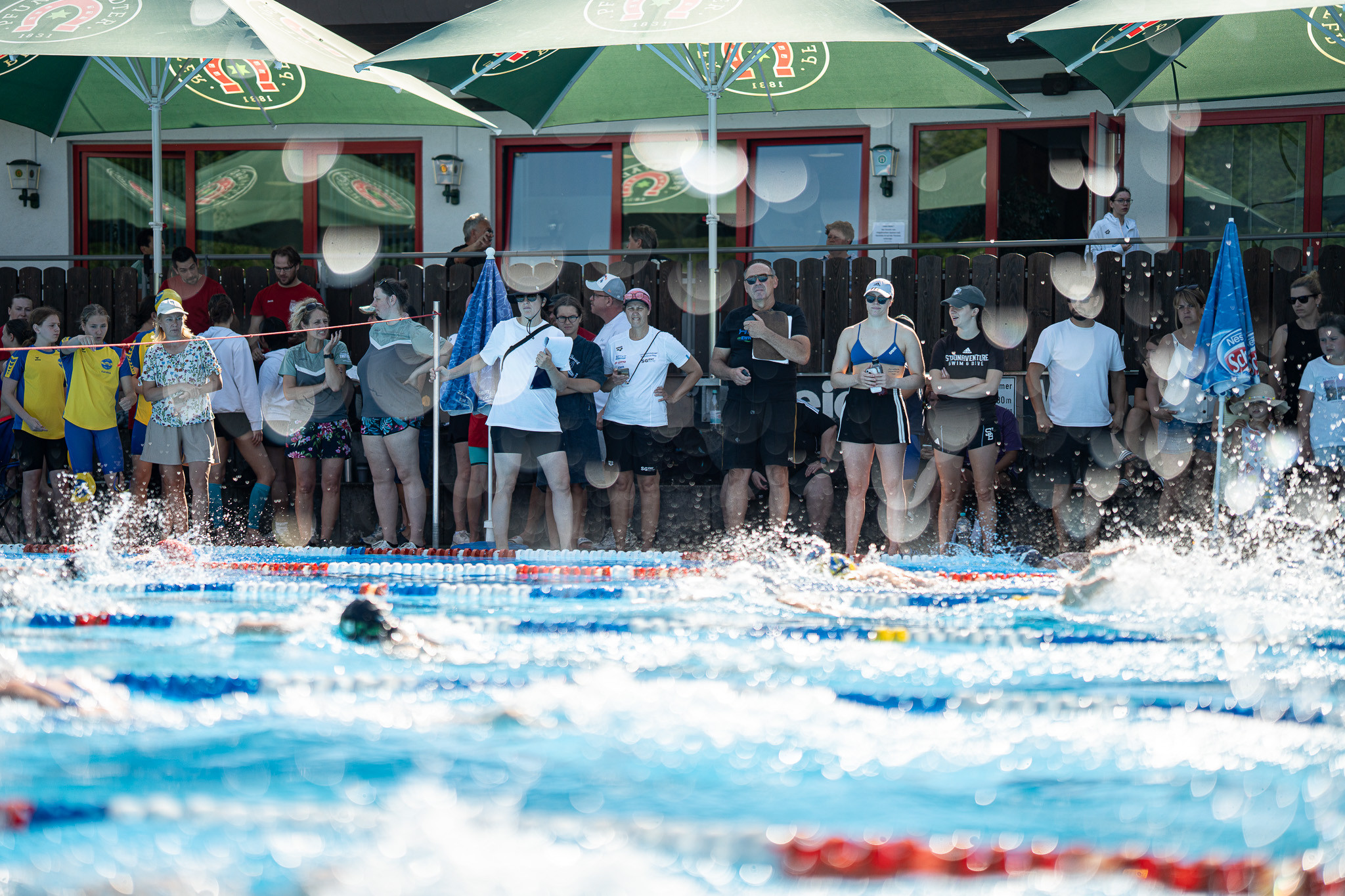 Zuschauer und Trainer am Beckenrand bei einem Schwimmwettkampf im Freibad
