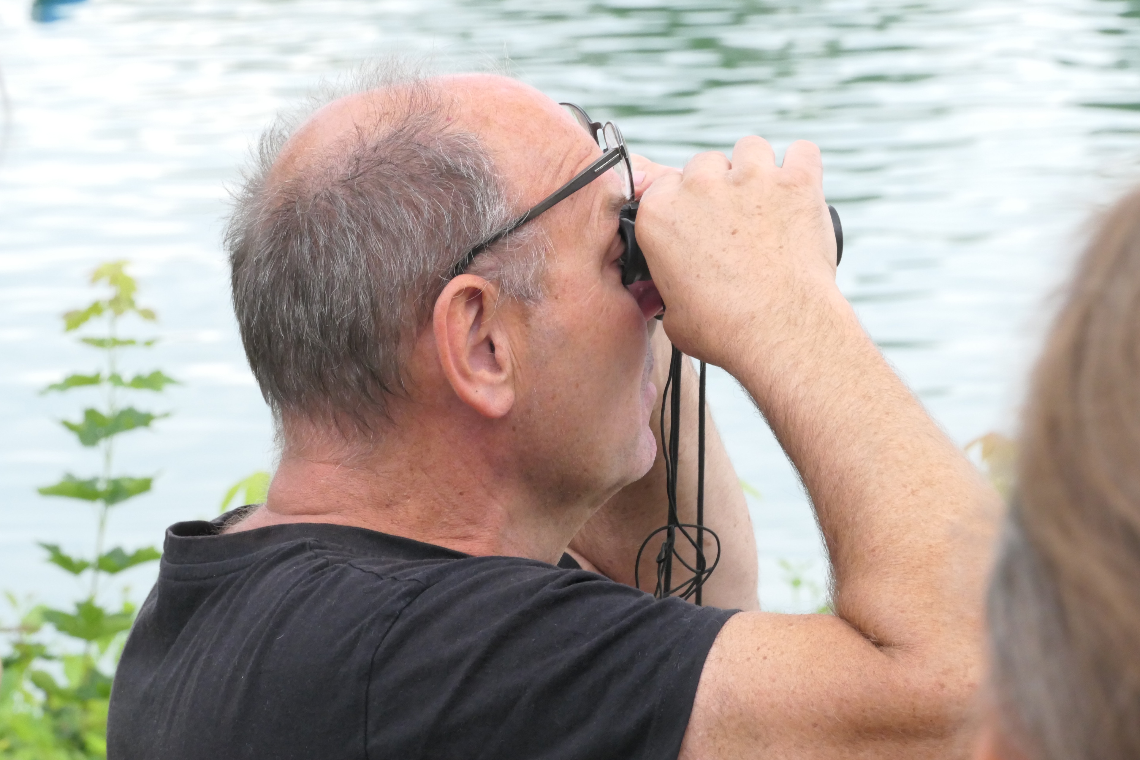 Mann beobachtet mit Fernglas am Wasser