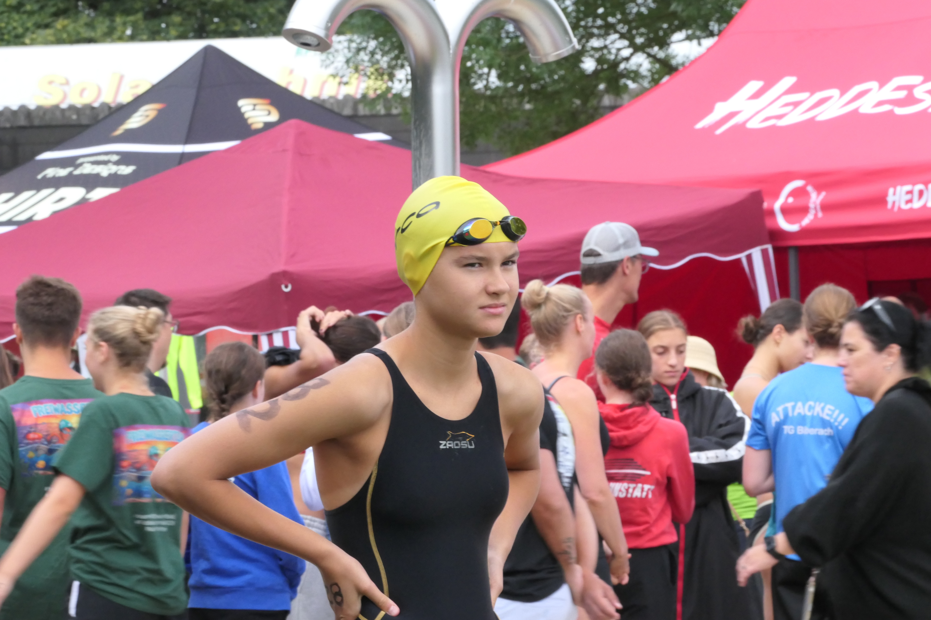 Schwimmerin mit gelber Badekappe und Schwimmbrille bei einem Wettkampf vor roten Zelten